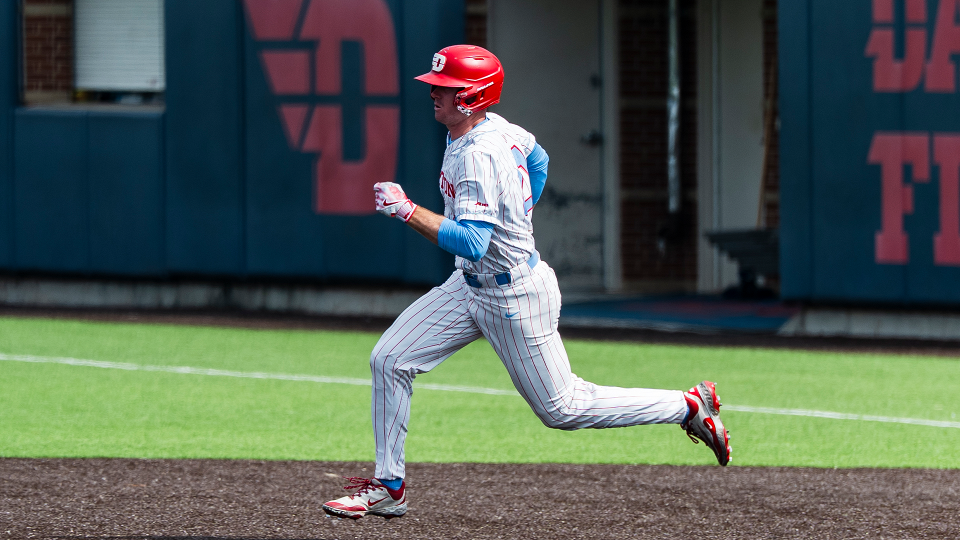 Danny MacDougall runs from first to second base. He is wearing a white pinstripe uniform and a red helmet.