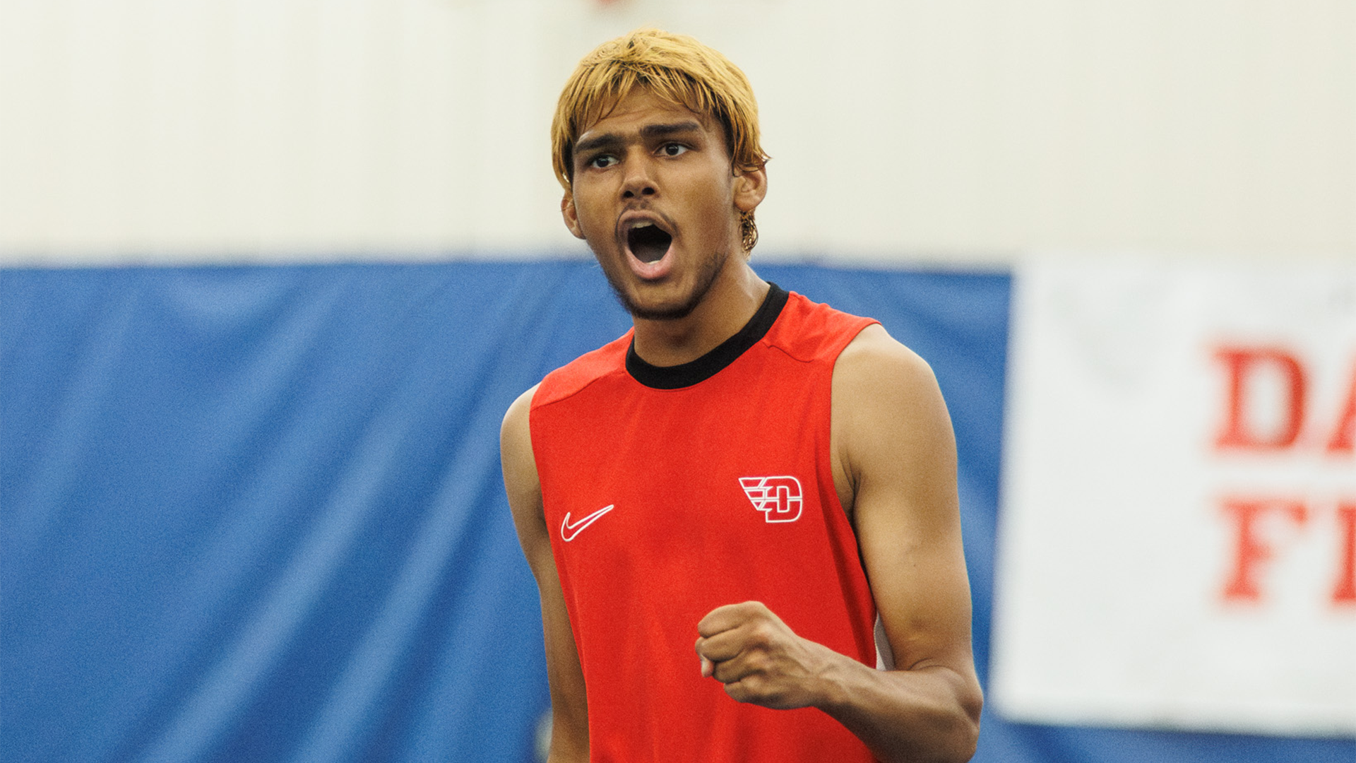 Rishi Dore, wearing a red tank top, yells and pumps his left fist.