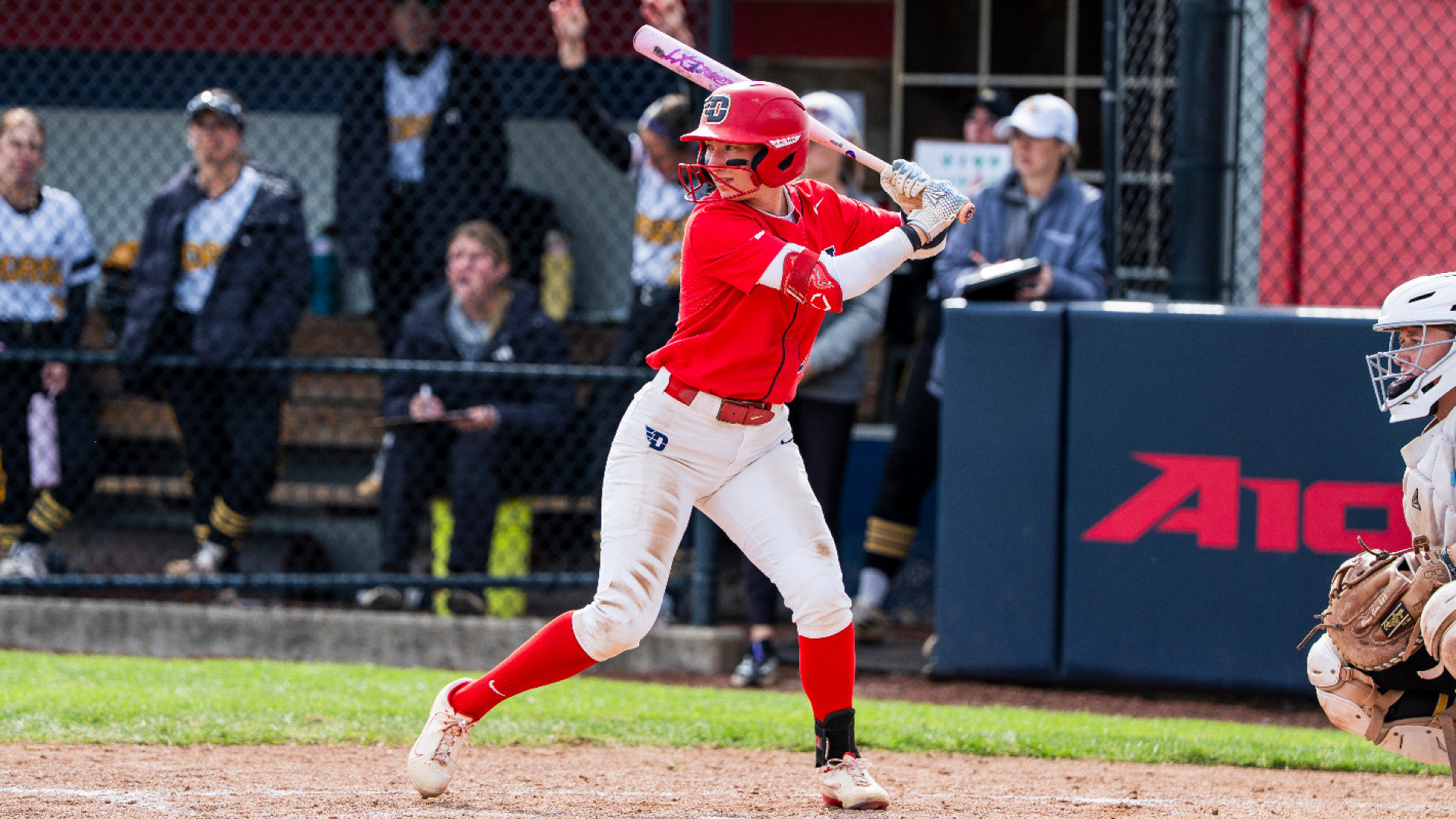 Softball's Kirnan Bailey, wearing a red uniform top with white pants, red socks and red batting helmet, stands in the batter's box with her bat over her left shoulding awaiting a pitch during a game at UD Softball Stadium