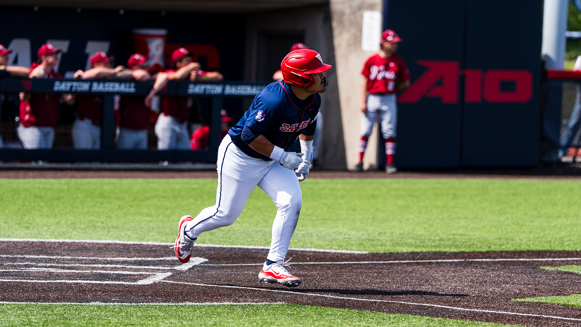 Dyrenson Wouters runs from the right-handed batter's box towards first base, watching for where the ball lands. He is wearing a red helmet, a navy jersey and white pants.