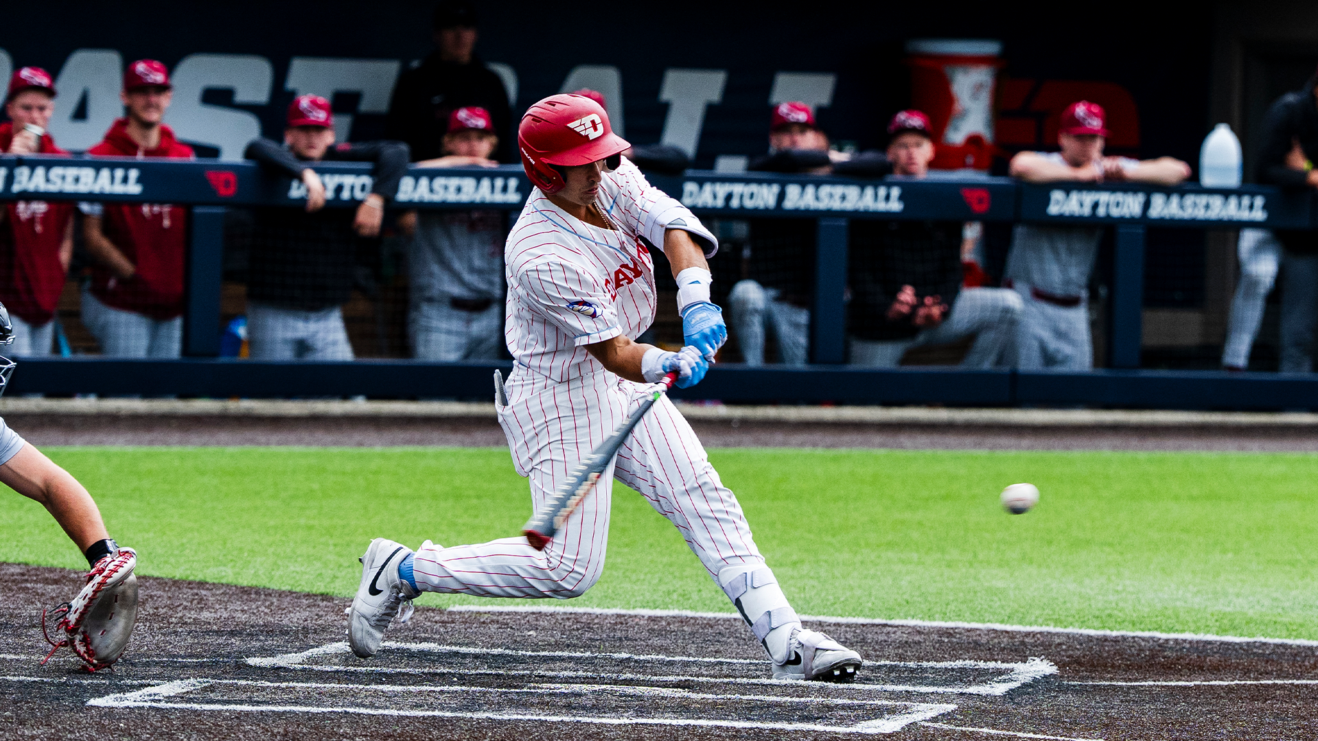 Jason Bello, wearing a white uniform and a red helmet, swings his bat at the incoming pitch.