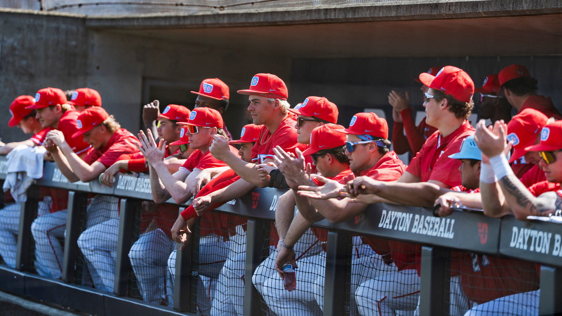Players in red uniforms clap while standing at the dugout railing.