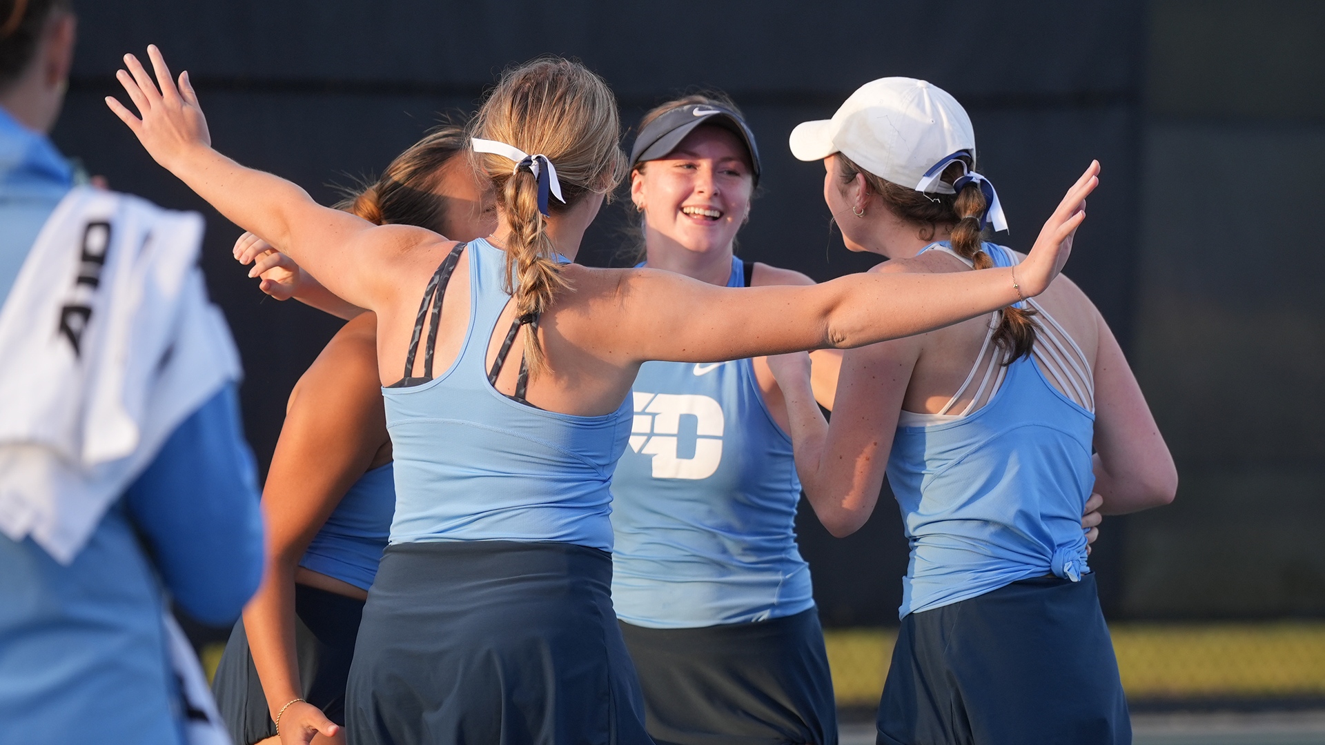 Baby Jordan, wearing a navy visor and light blue tank top, celebrates with her teammates after winning the clinching match.