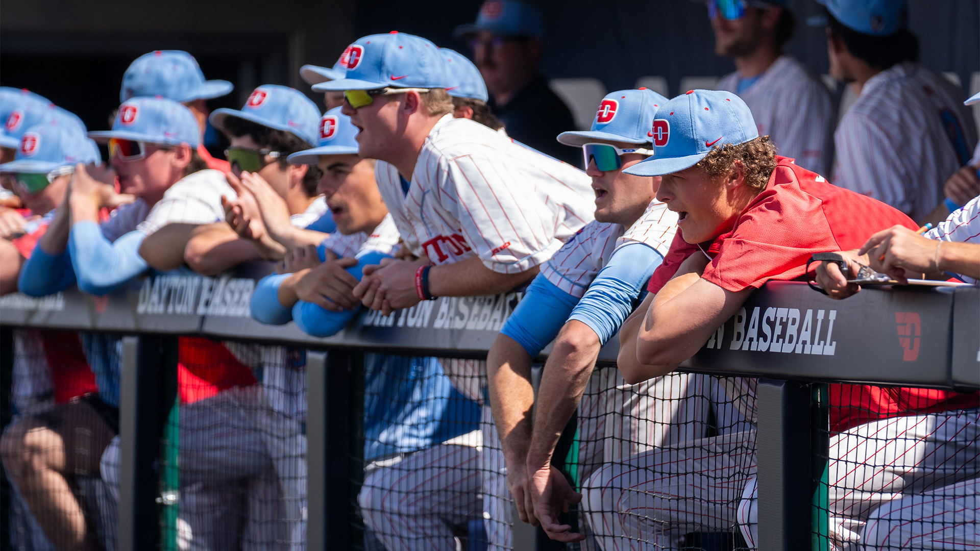 Players hang on the dugout railing, yelling and cheering on the players on the field.