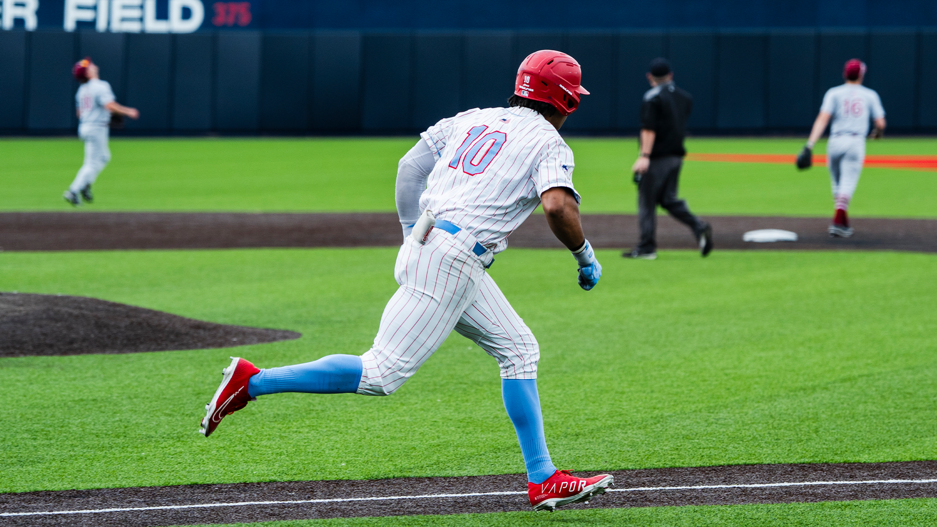 Michael Smith Jr., wearing a white pinstripe uniform and a red helmet, runs from the batter's box to first base.