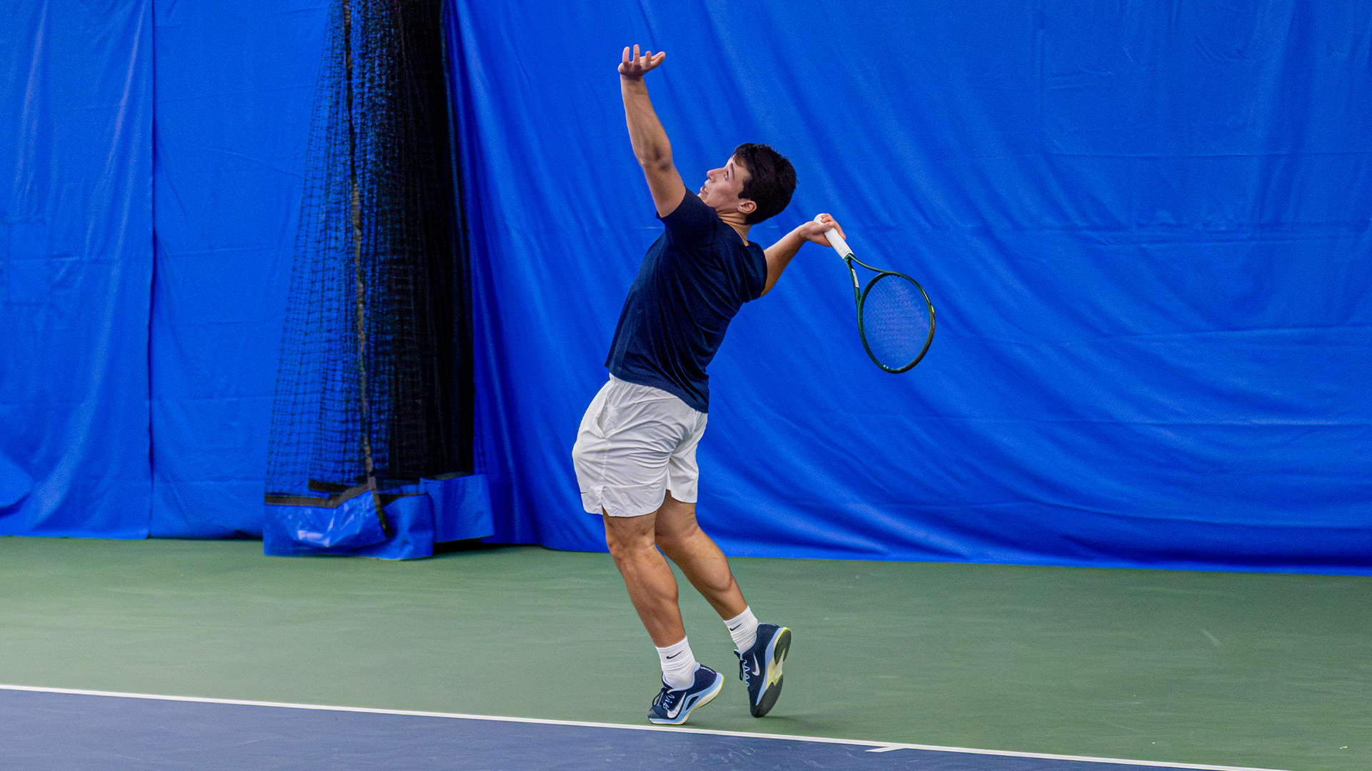 Mikkel Zinder throws a ball in the air with his left hand, winding his racquet back in his right to serve.