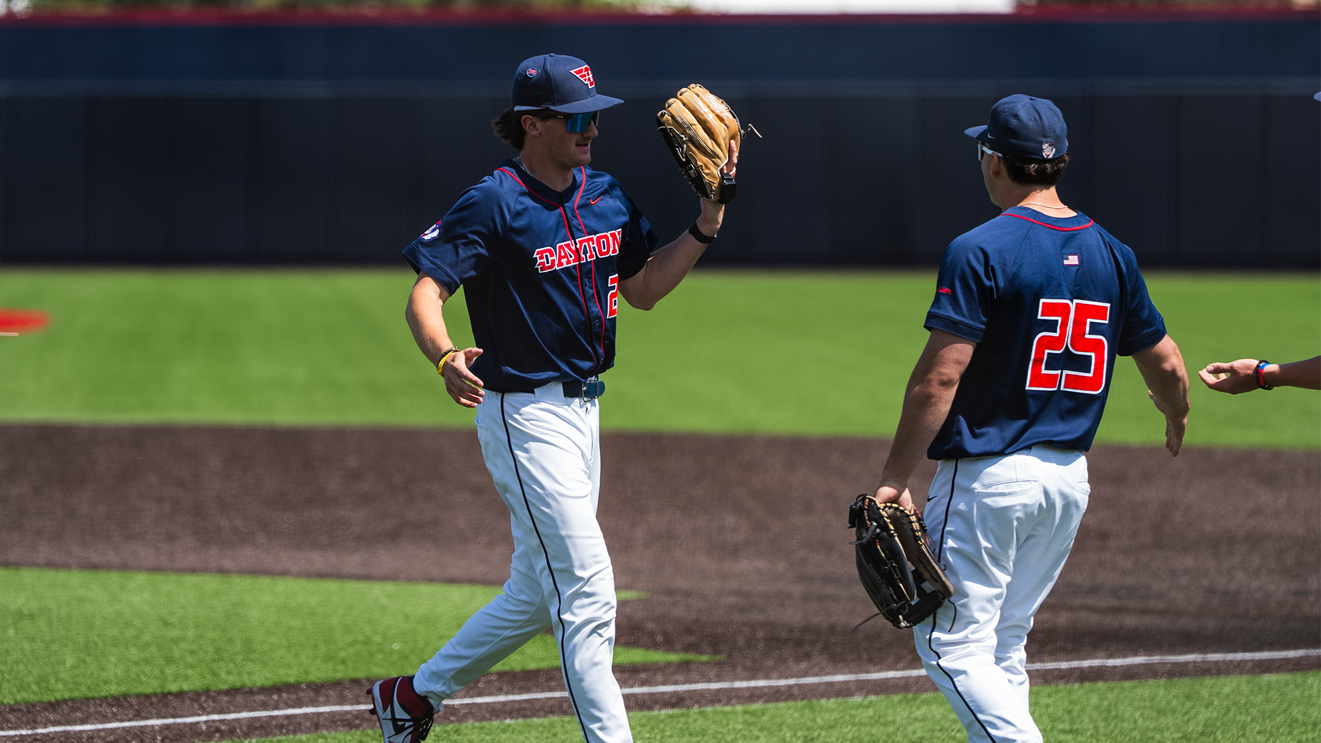 Colin Lynch jogs off the field, high fiving Grayson Carpenter. They are both wearing a navy jersey and white pants.