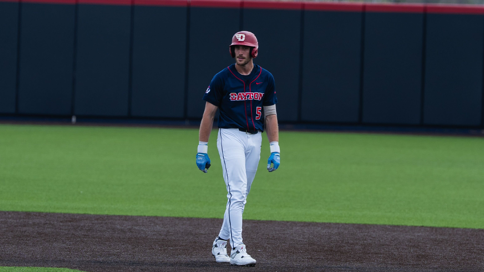 Aiden Heberlie, wearing a navy uniform and a red helmet, walks back to second base from third.