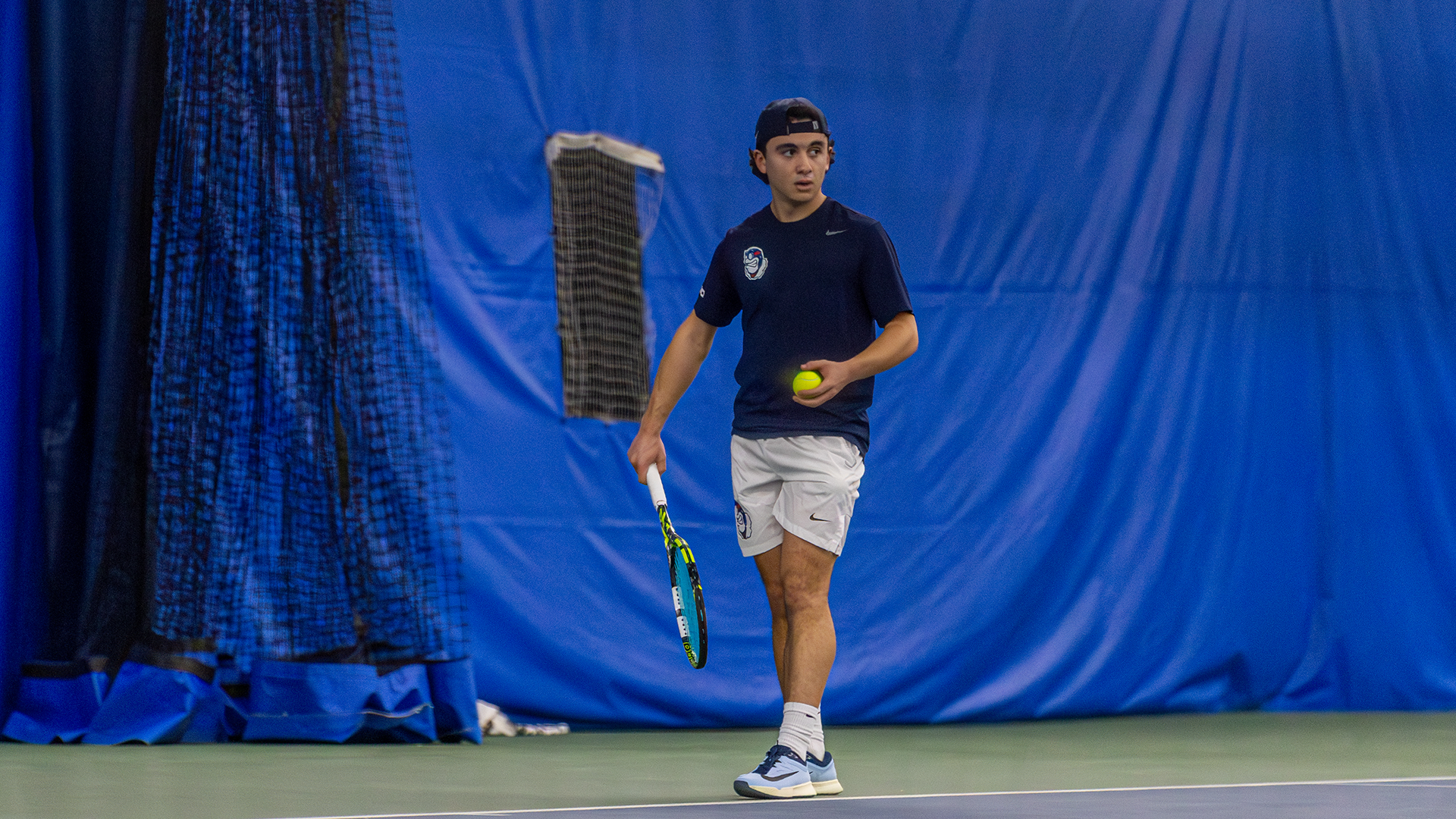 Dylan Jaen holds his racquet in his right hand and a ball his left, looking towards his opponent.