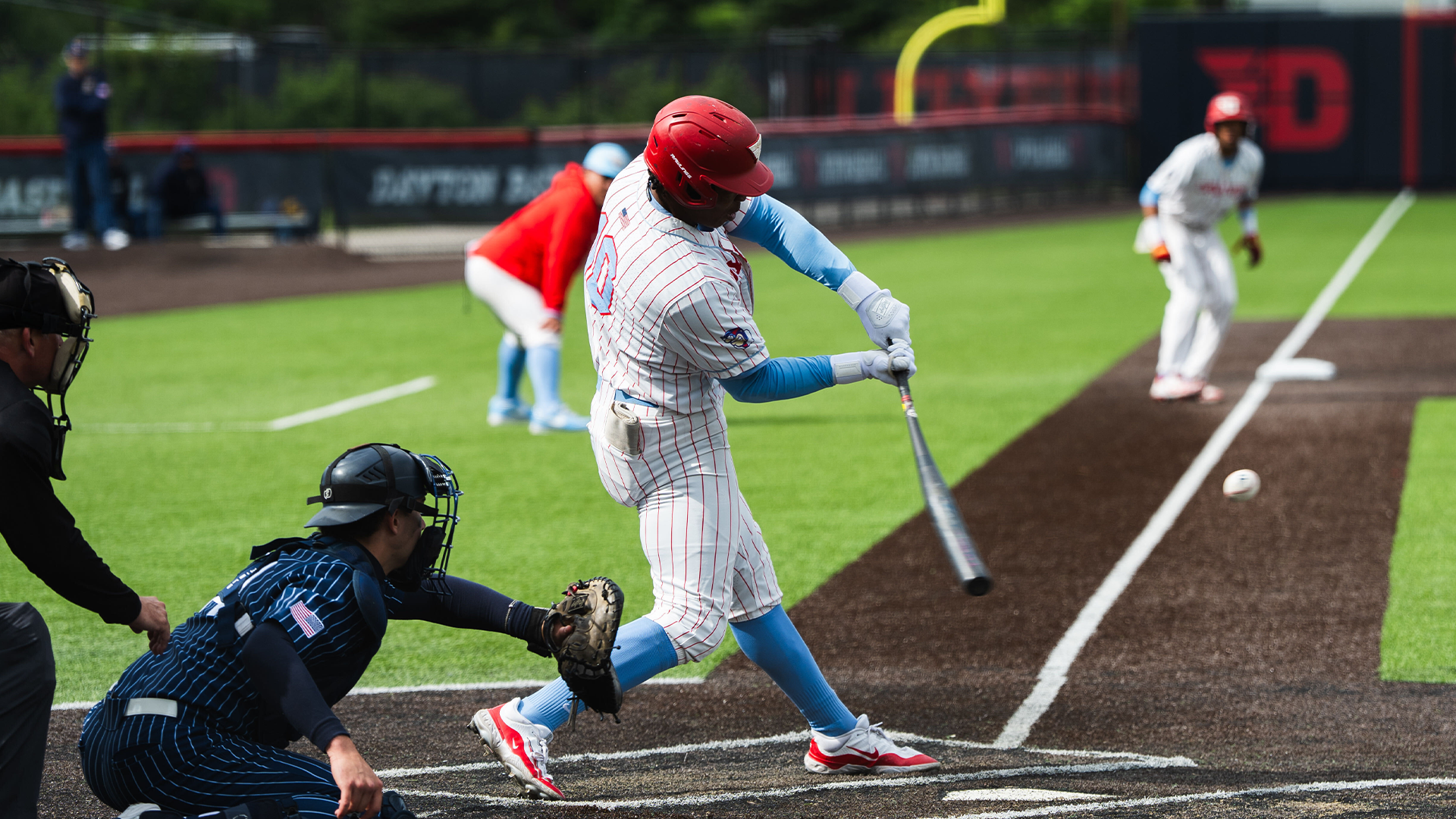 Michael Smith Jr. hits the ball. He is in the right-handed batter's box and is wearing a white, pinstripe uniform and a red helmet.