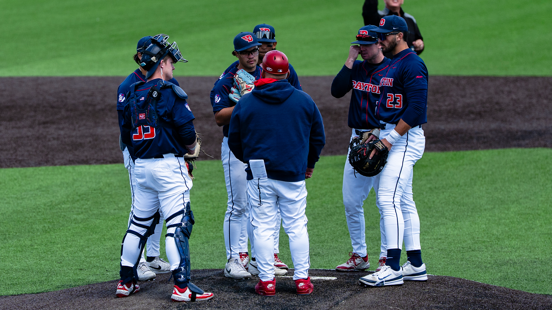 The infield huddles with Jayson King as he talks to John Delgado. They are all wearing navy shirts and white pants.