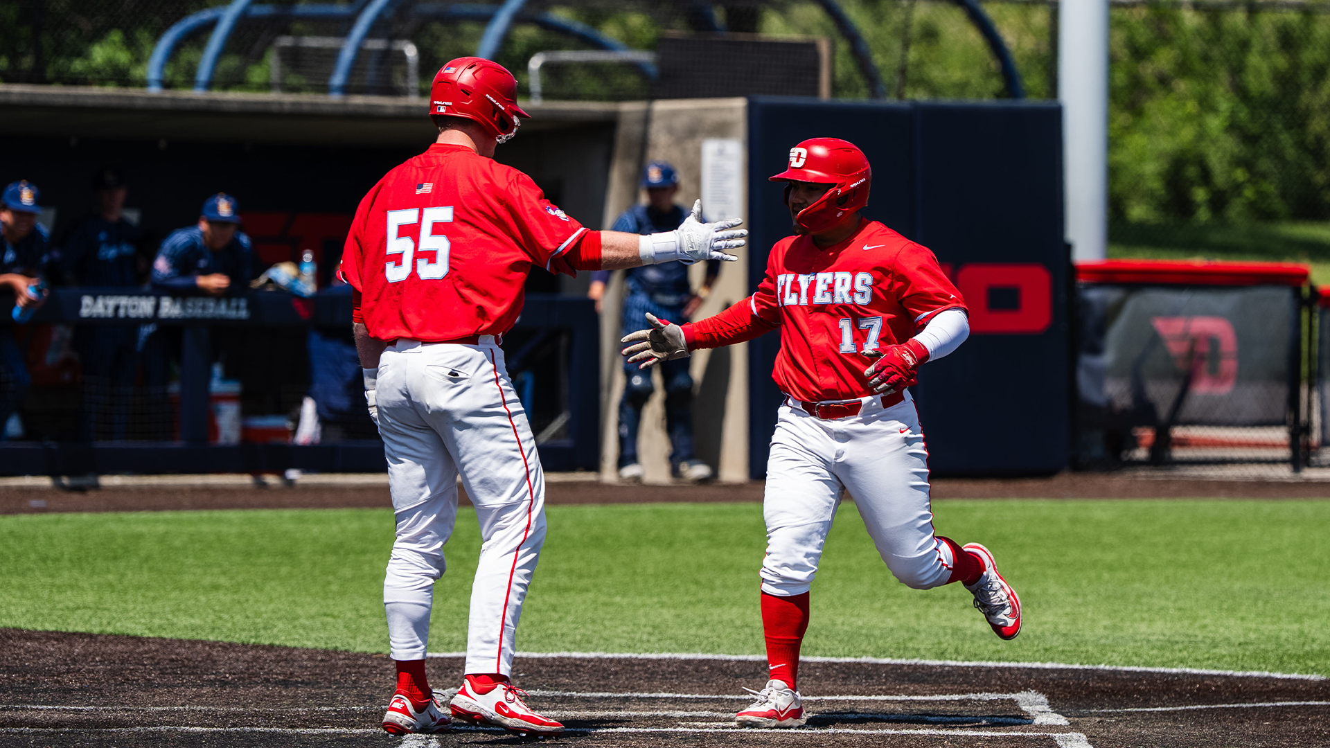 Wearing red jerseys and helmets with white pants, Dyrenson Wouters and Ryan MacDougall celebrate Wouters scoring a run.