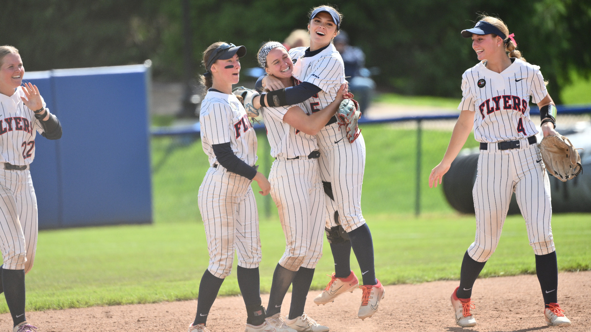 Members of the softball team, wearing pinstripe uniforms and navy softs, celebrate near the circle during a game