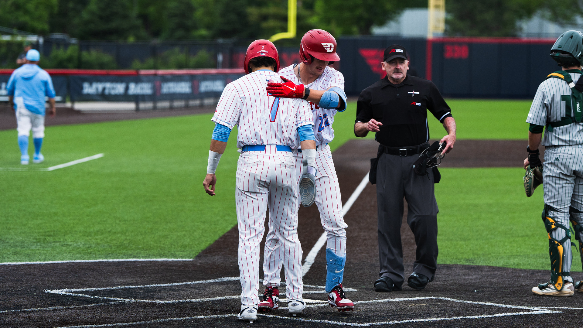 Jason Bello and Colin Lynch hug at home plate. Both are wearing a white pinstripe uniform and red helmets.