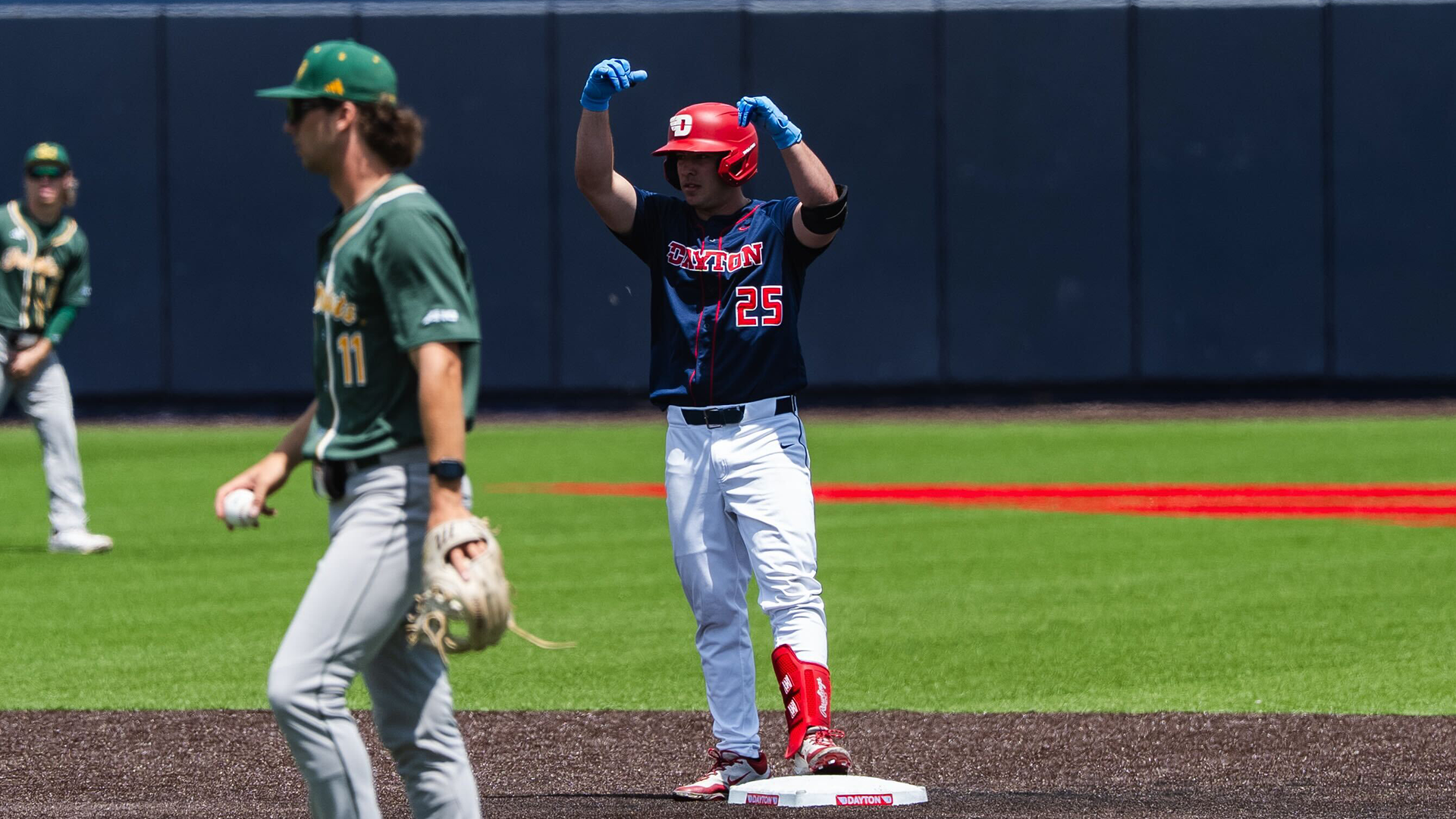 Grayson Carpenter stands on second base with his hands above his head in celebration. He is wearing a red helmet, a navy jersey, white pants and Chapel Blue gloves.