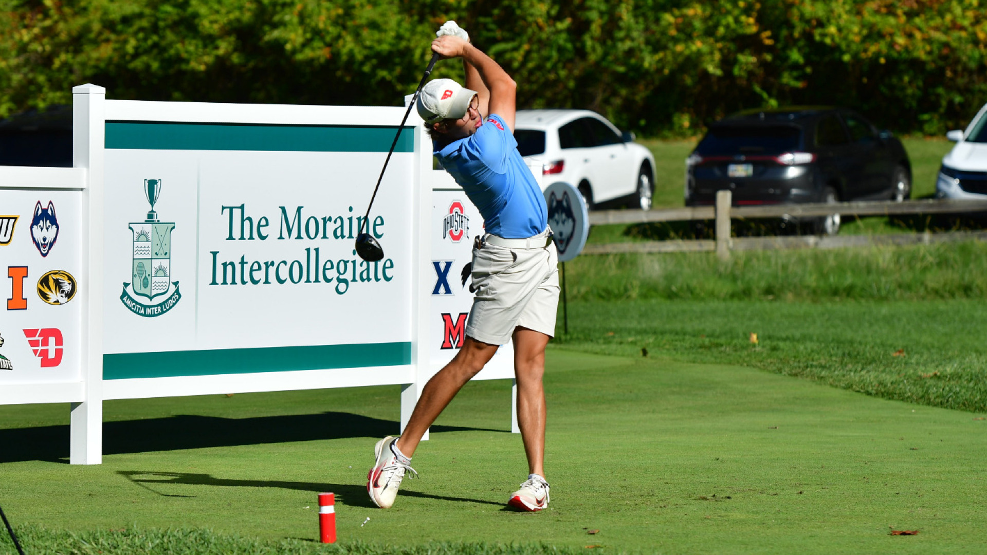 Men's golfer Brekin Taylor, wearing a light blue polo-style shirt, khaki colored shorts and a white hat with a red winged-D logo, tees off during the 2025 Moraine Intercollegiate