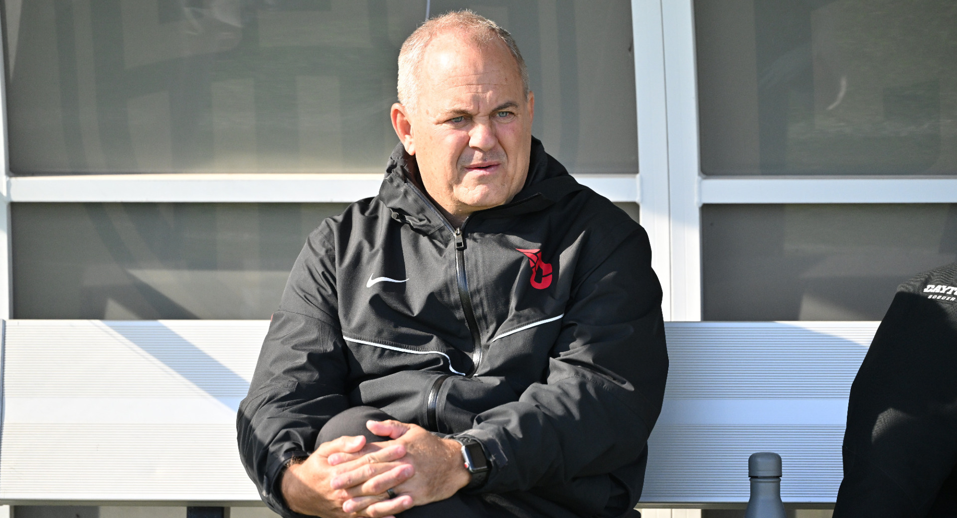 Men's soccer head coach Dennis Currier sitting on the bench looking out on the field ahead of the Flyers' 2025 A-10 Championship title game at Saint Louis