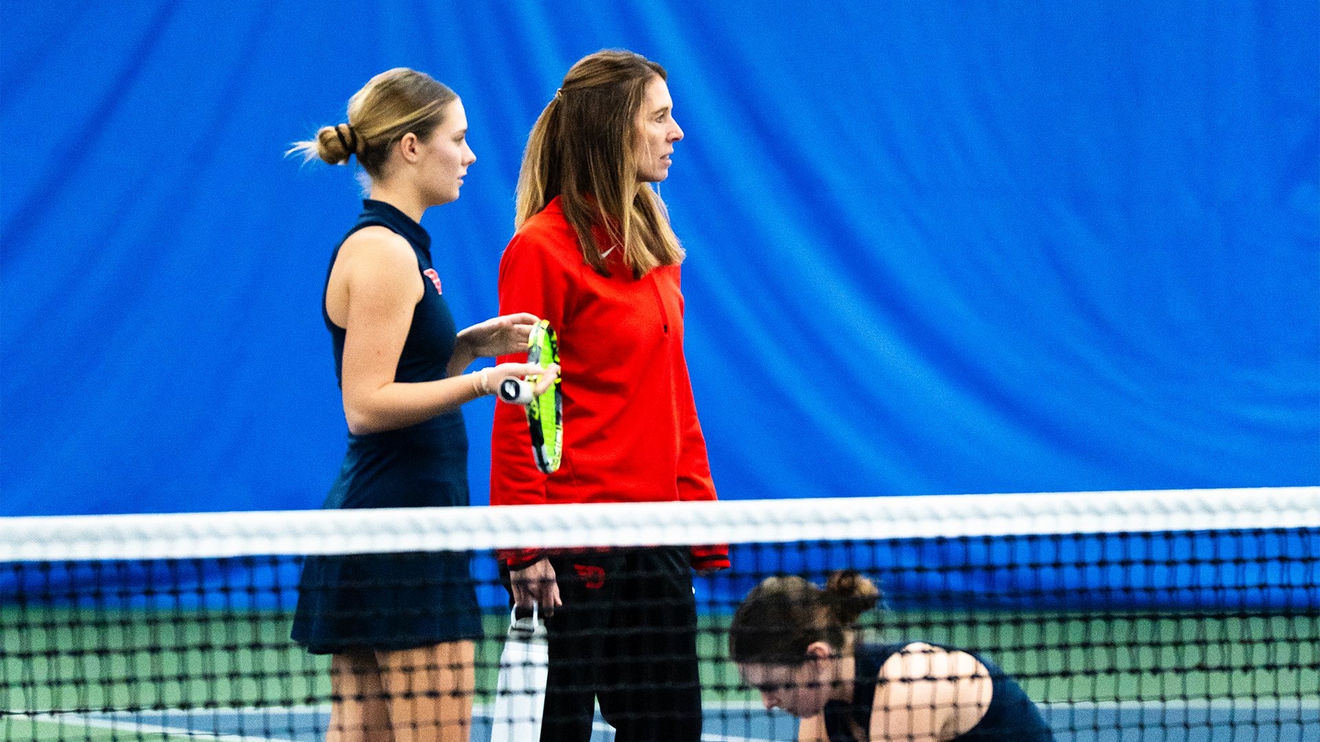 Erica Echko, wearing a red quarterzip, talks to Mallory Hitchcock and Baby Jordan.