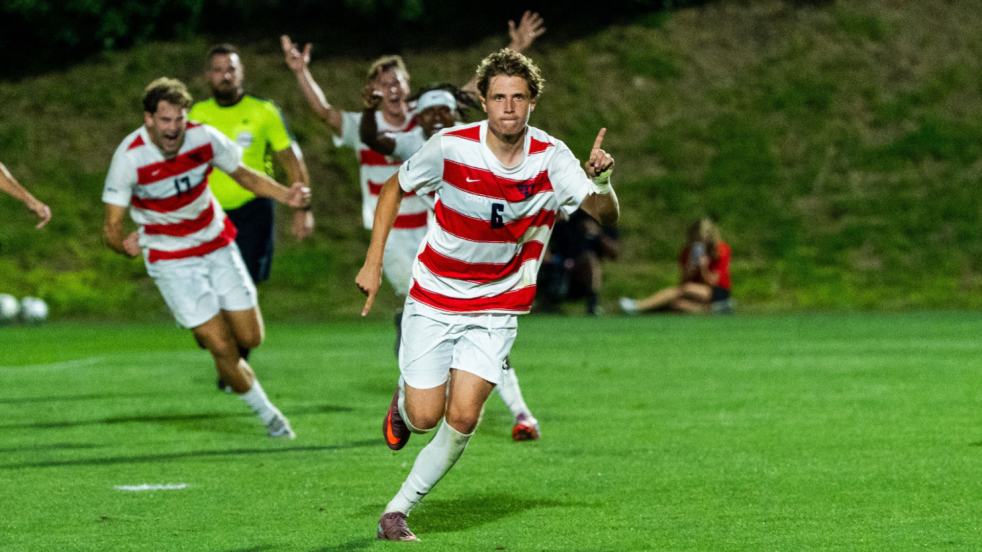 Men's soccer player Mikkel Madsen, wearing a red and white stripped jersey, white shorts and white socks, holds up his index finger in celebration after a goal in a match at Baujan Field