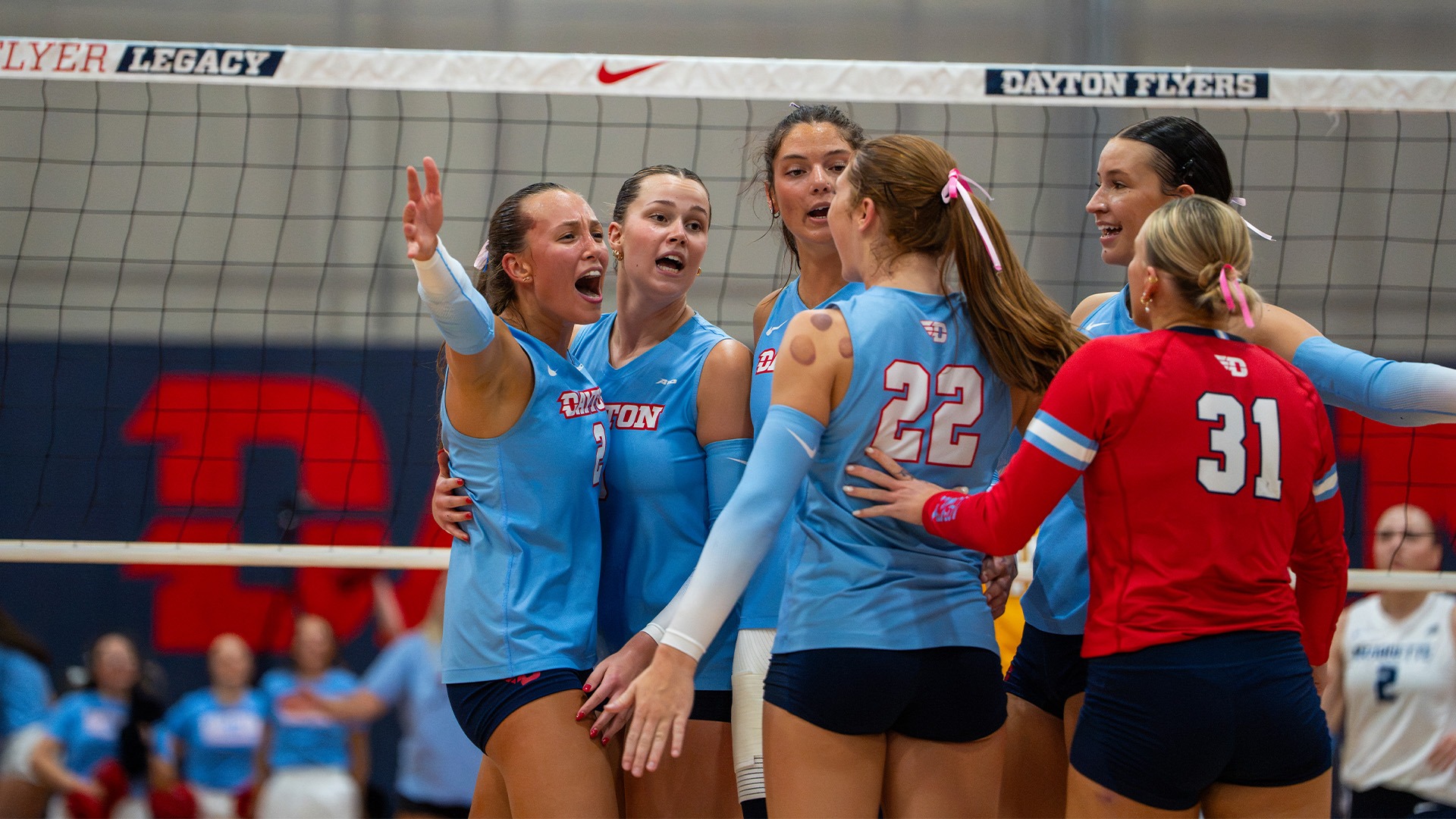 Teammates celebrate Sidney Sprada after a point. The team is in chapel blue uniforms, while the libero is in red.