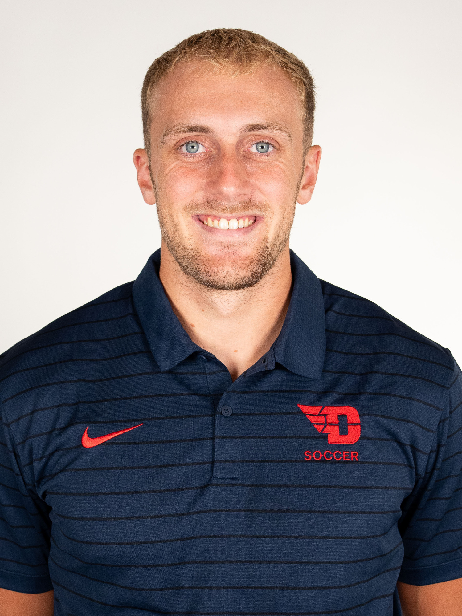 Portrait image of Freddy Rogers wearing a blue polo-style shirt with a red Nike logo and a red flying D logo with the word soccer under it