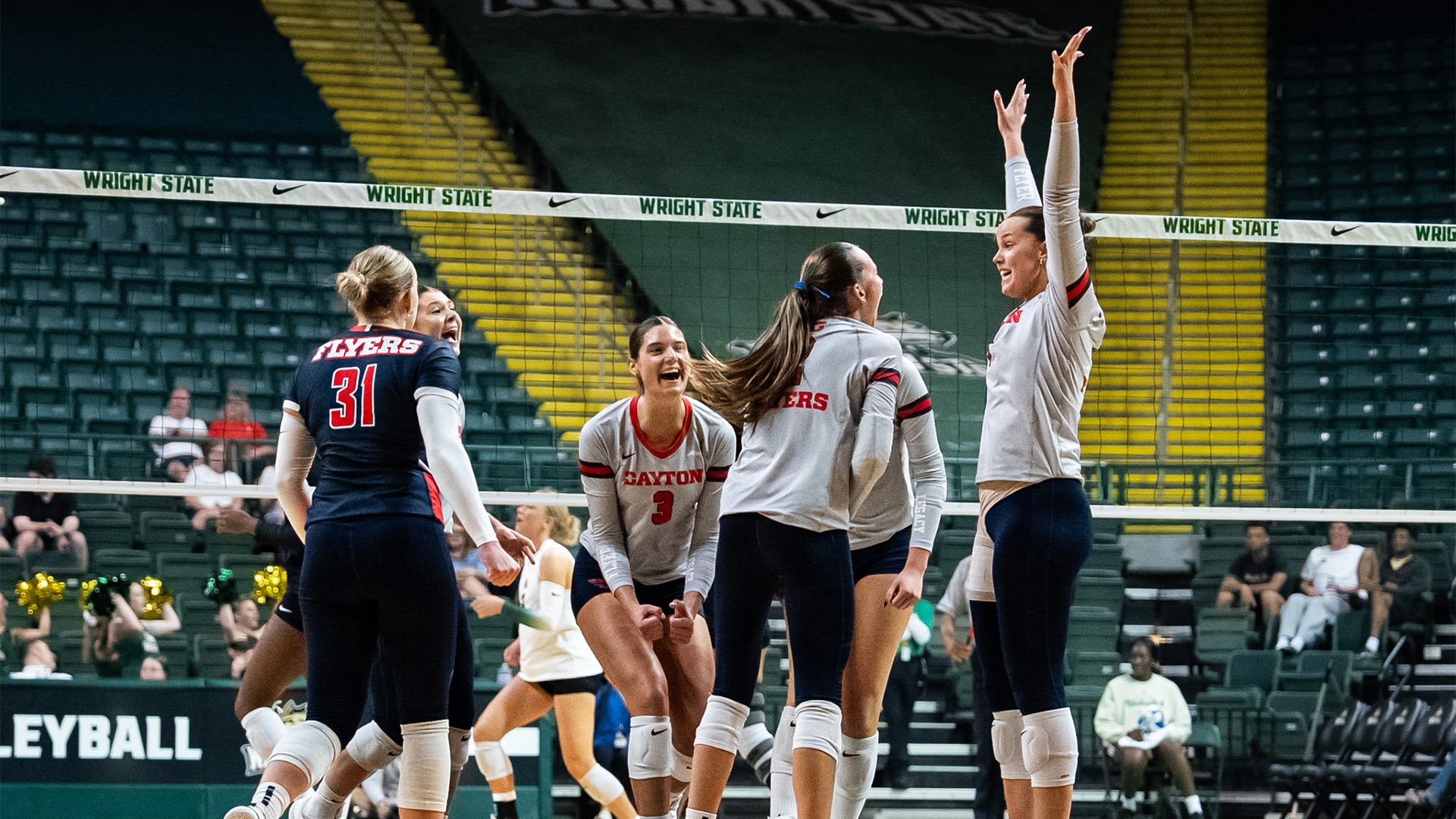 Volleyball players celebrate after a point. They are wearing grey uniforms and navy pants.