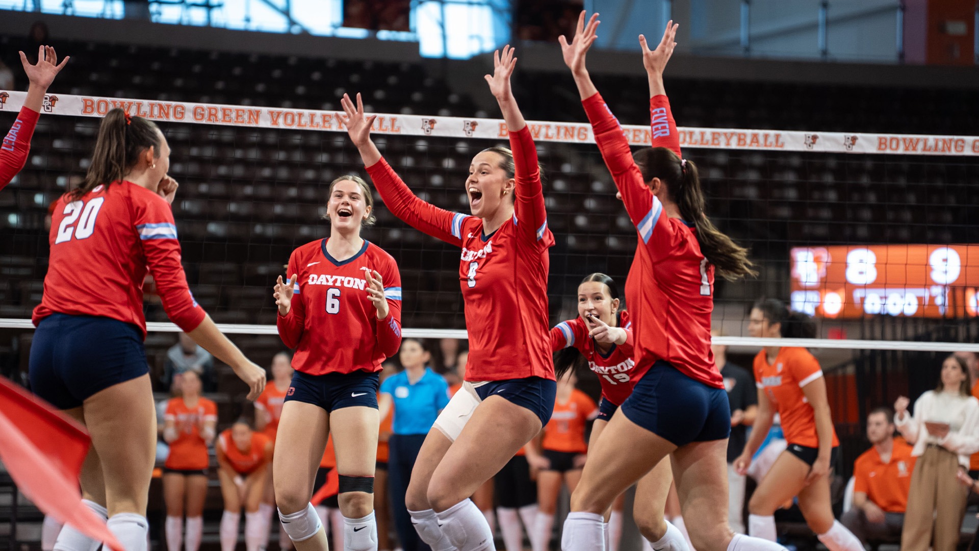 Volleyball players celebrate after a point. They are wearing red uniforms and navy shorts.