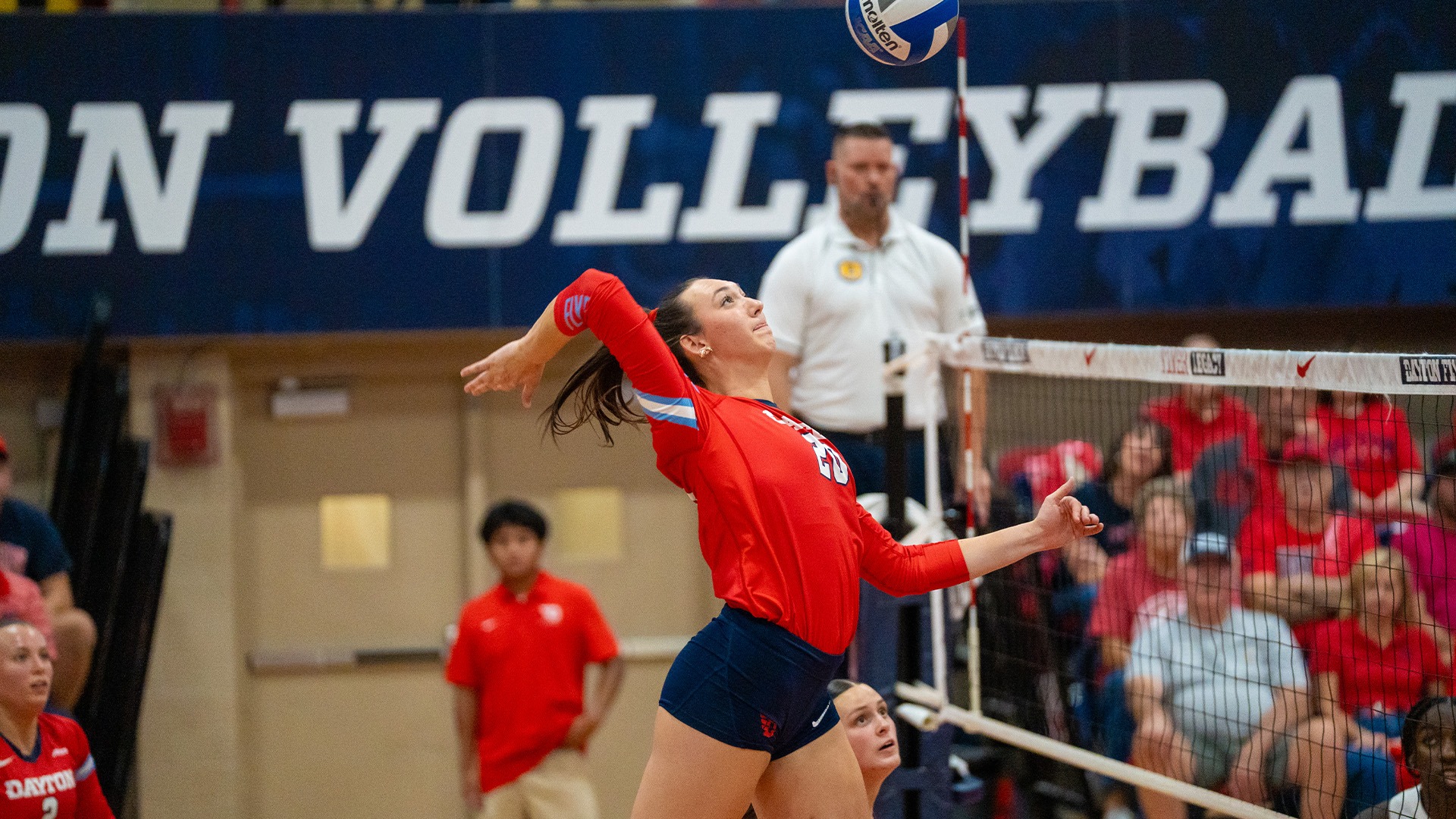 Ava Liening swings at the ball at the net. She is wearing a red jersey and navy shorts.
