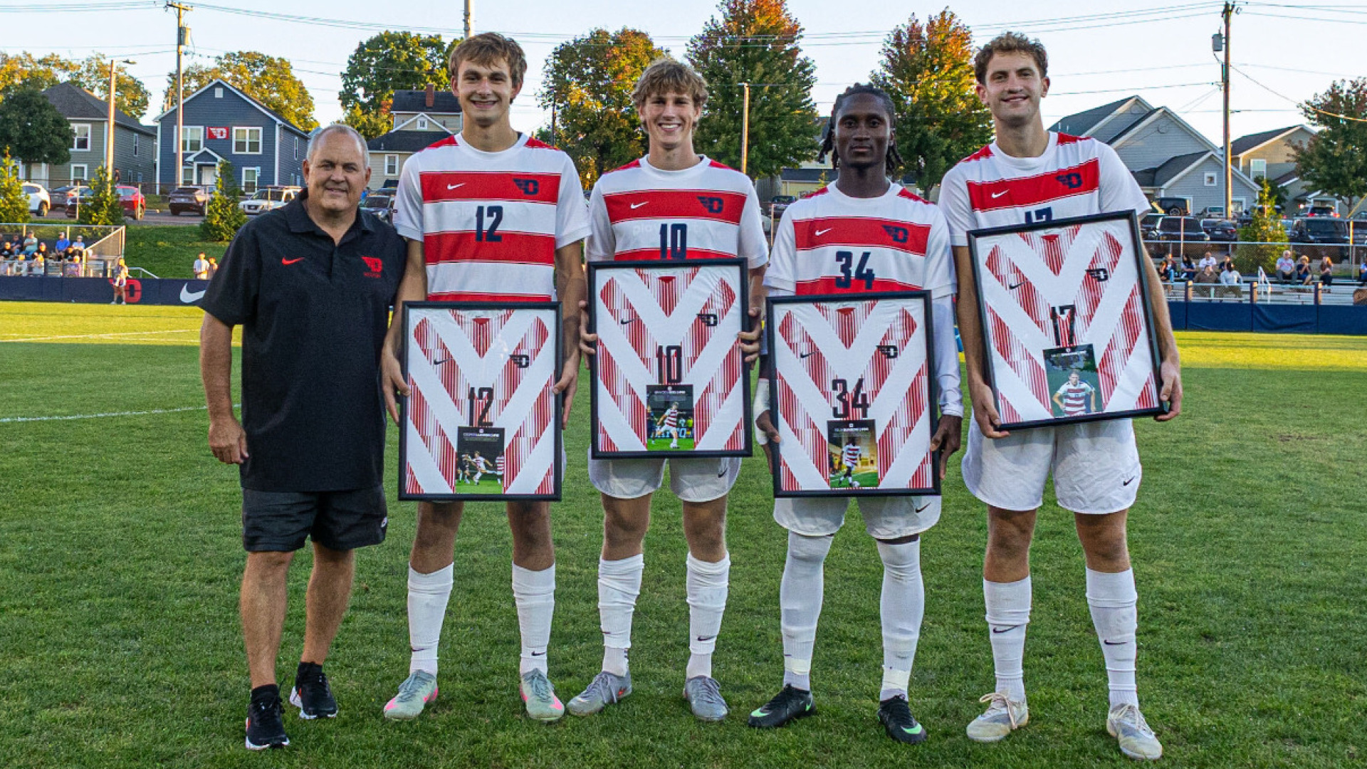 Men's soccer head coach Dennis currier stands with four senior team members holding framed jerseys during Senior Night at Baujan Field