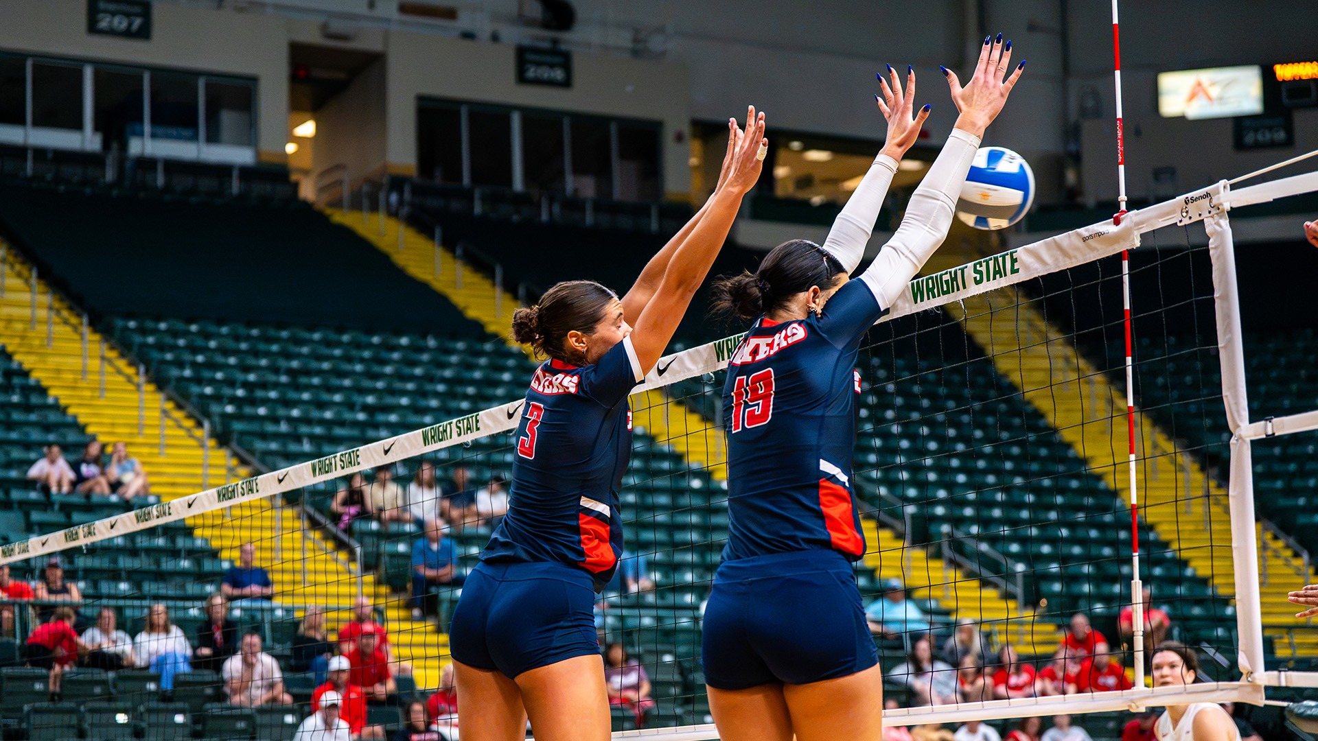 Abigail Cresse and Charlotte Vinson go up to block the ball. They are wearing navy uniforms.