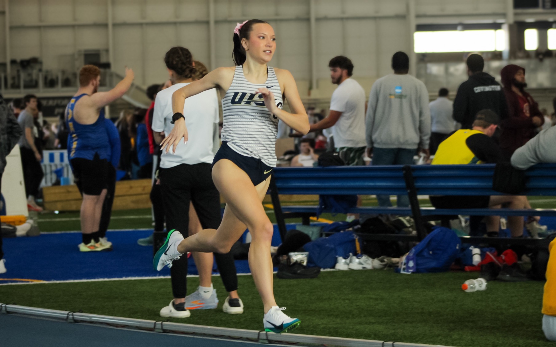 Madelyn Miller-Ross running indoor track in white UIS uniform