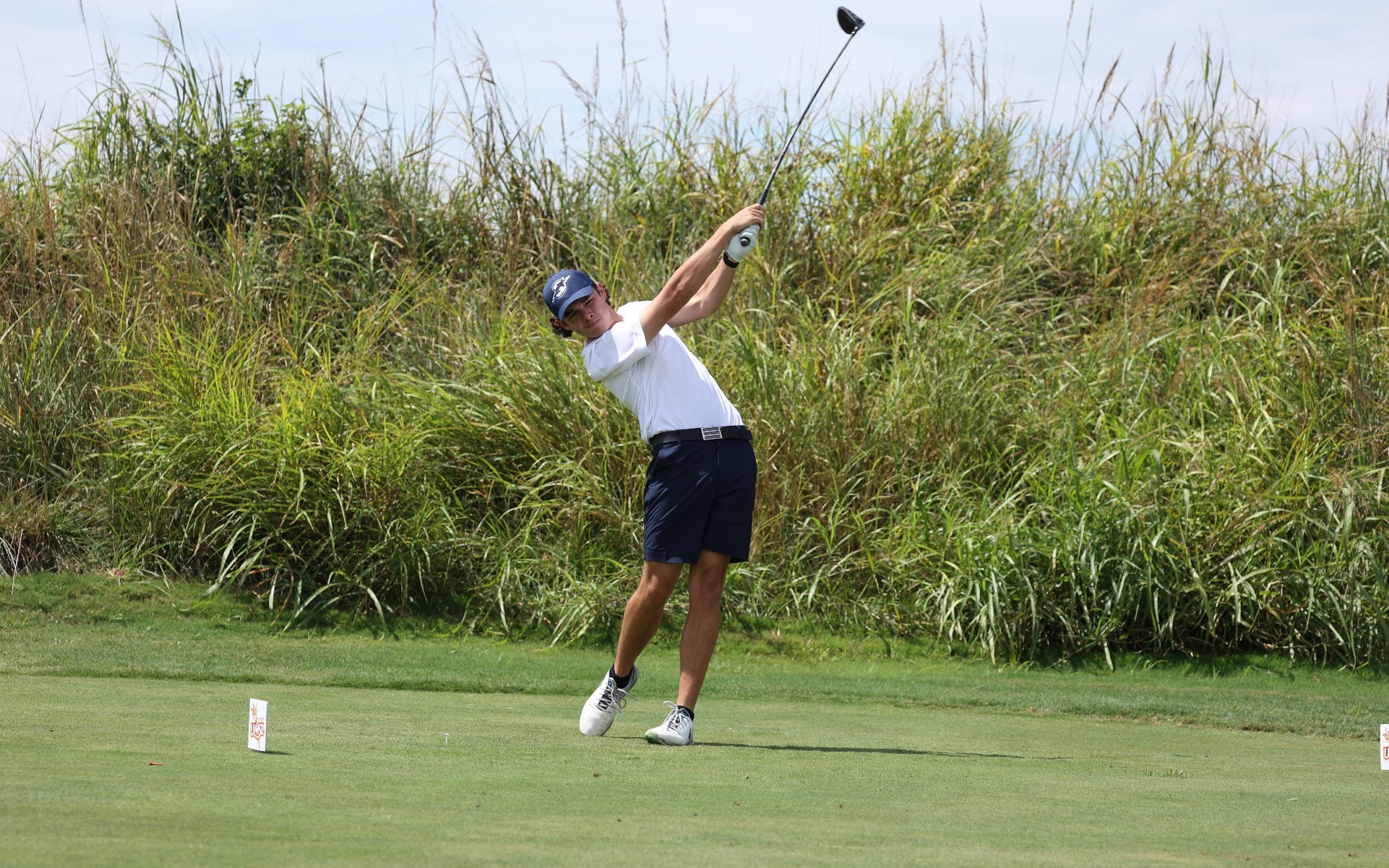 A photo of Jake Balding golfing in a white polo and blue hat