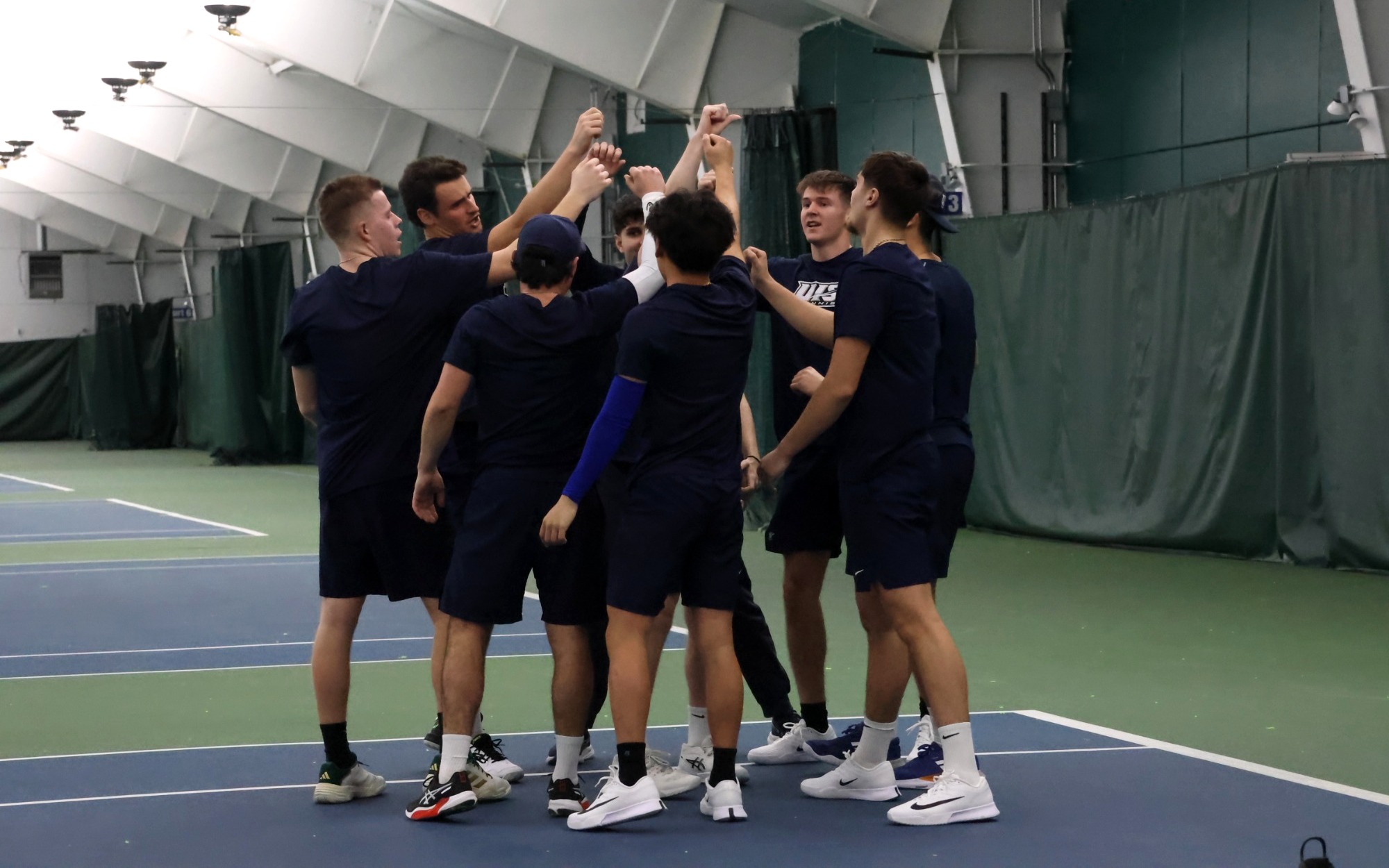 UIS men's tennis team in a huddle at indoor facility