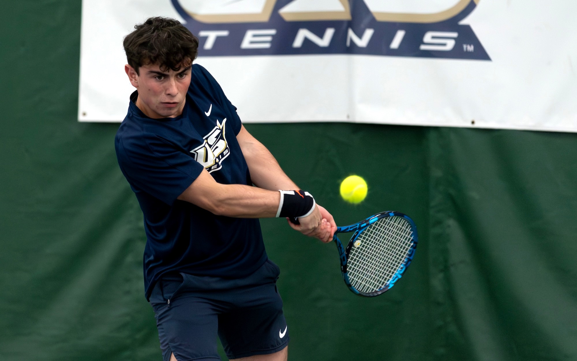 Pablo Herrera playing tennis indoors in blue UIS Uniform
