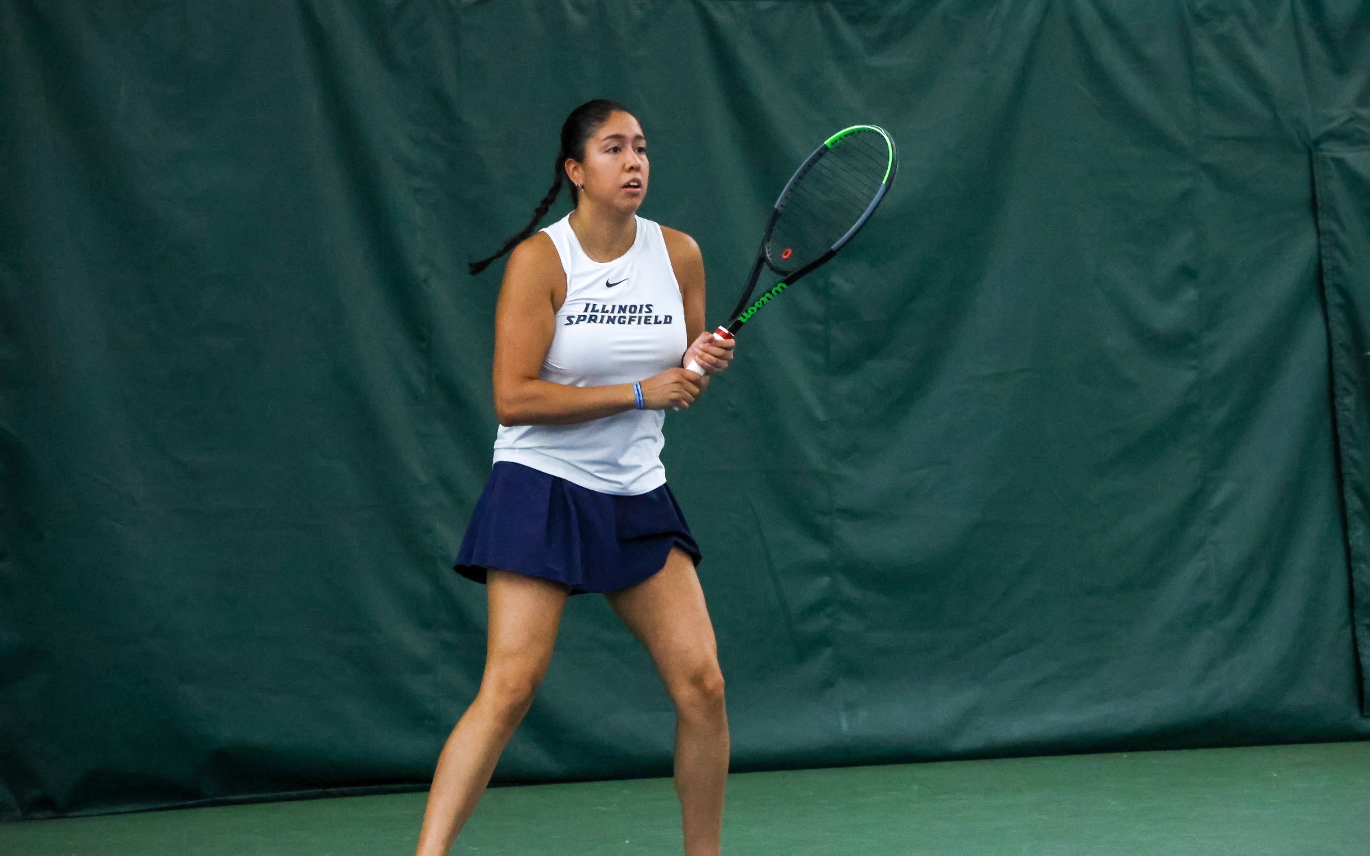 Cristina Mendoza Romero playing tennis indoors in white and blue UIS uniform