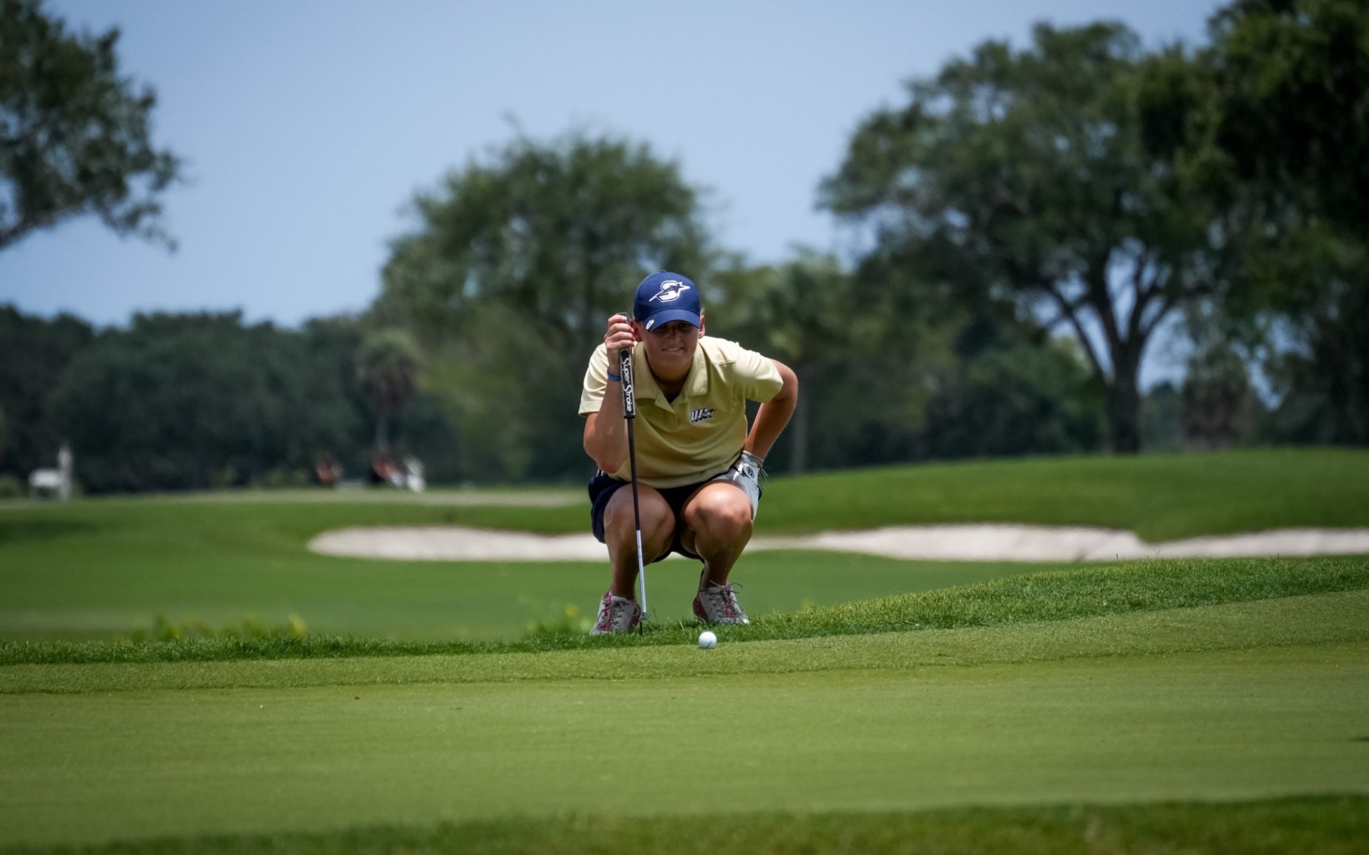 Elaine Grant in gold UIS polo and blue UIS hat golfing