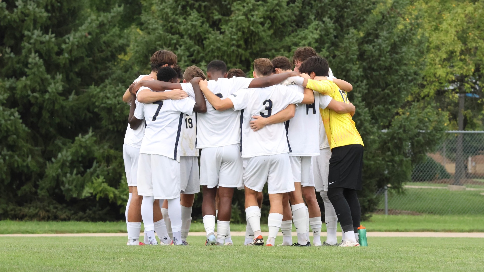 Men's Soccer Huddle on field pre-game, UIS players in white and yellow jerseys