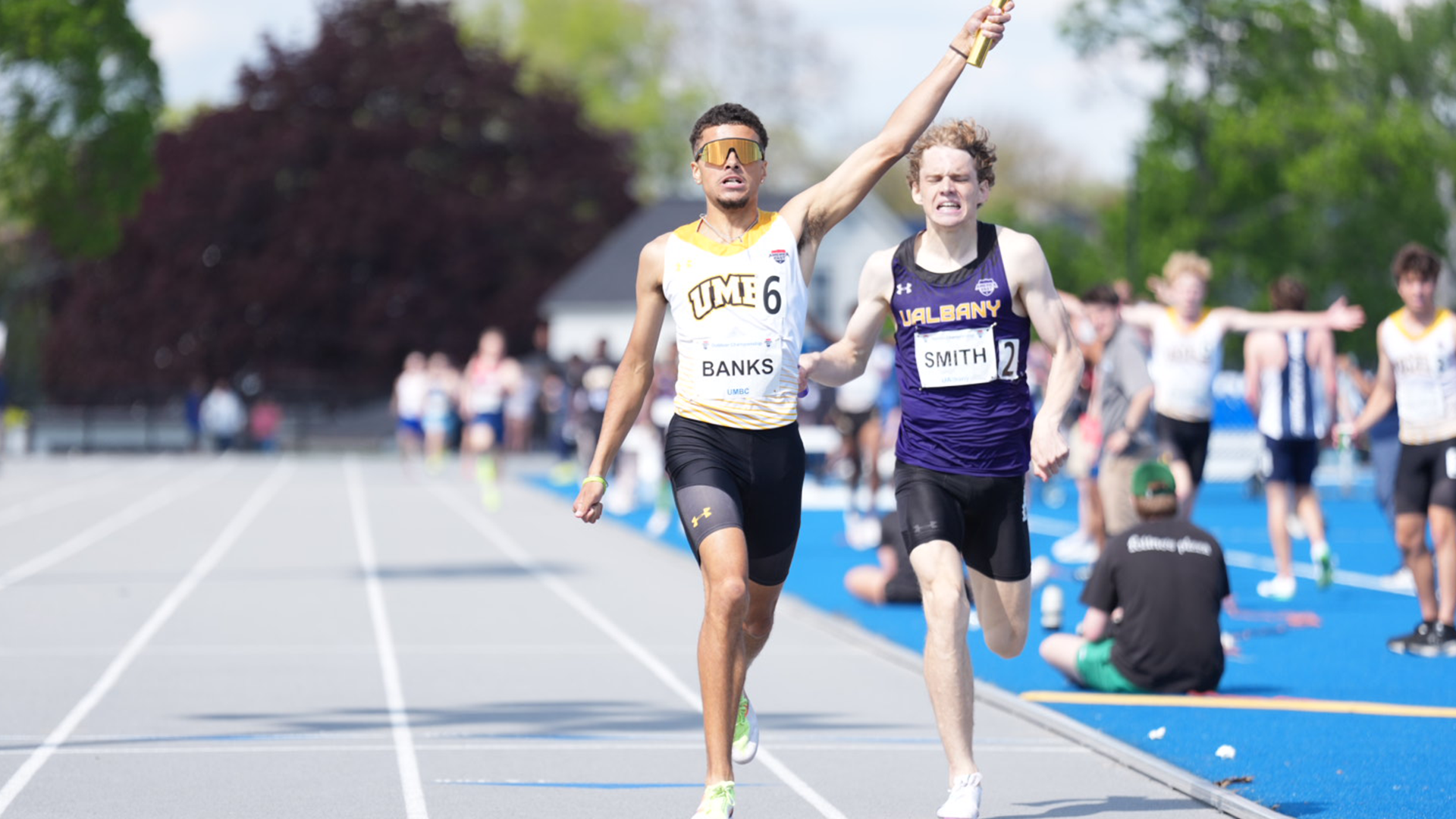 Justin Banks raises his gold baton in the air with his left hand as he celebrates winning the 4x800 meter relay at America East Outdoor Championships