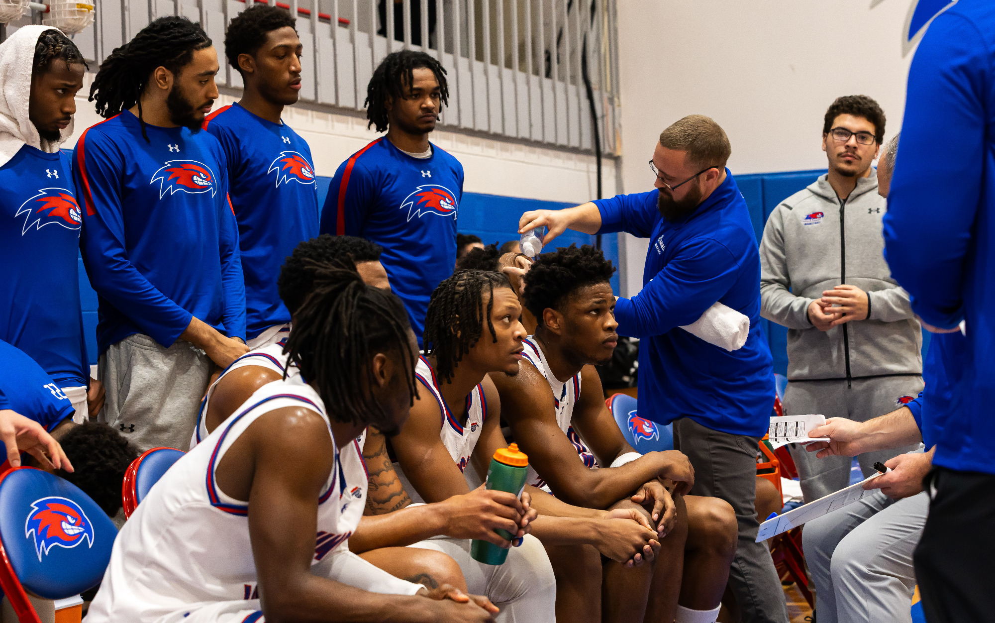 Men's basketball players meeting near the bench during a timeout.