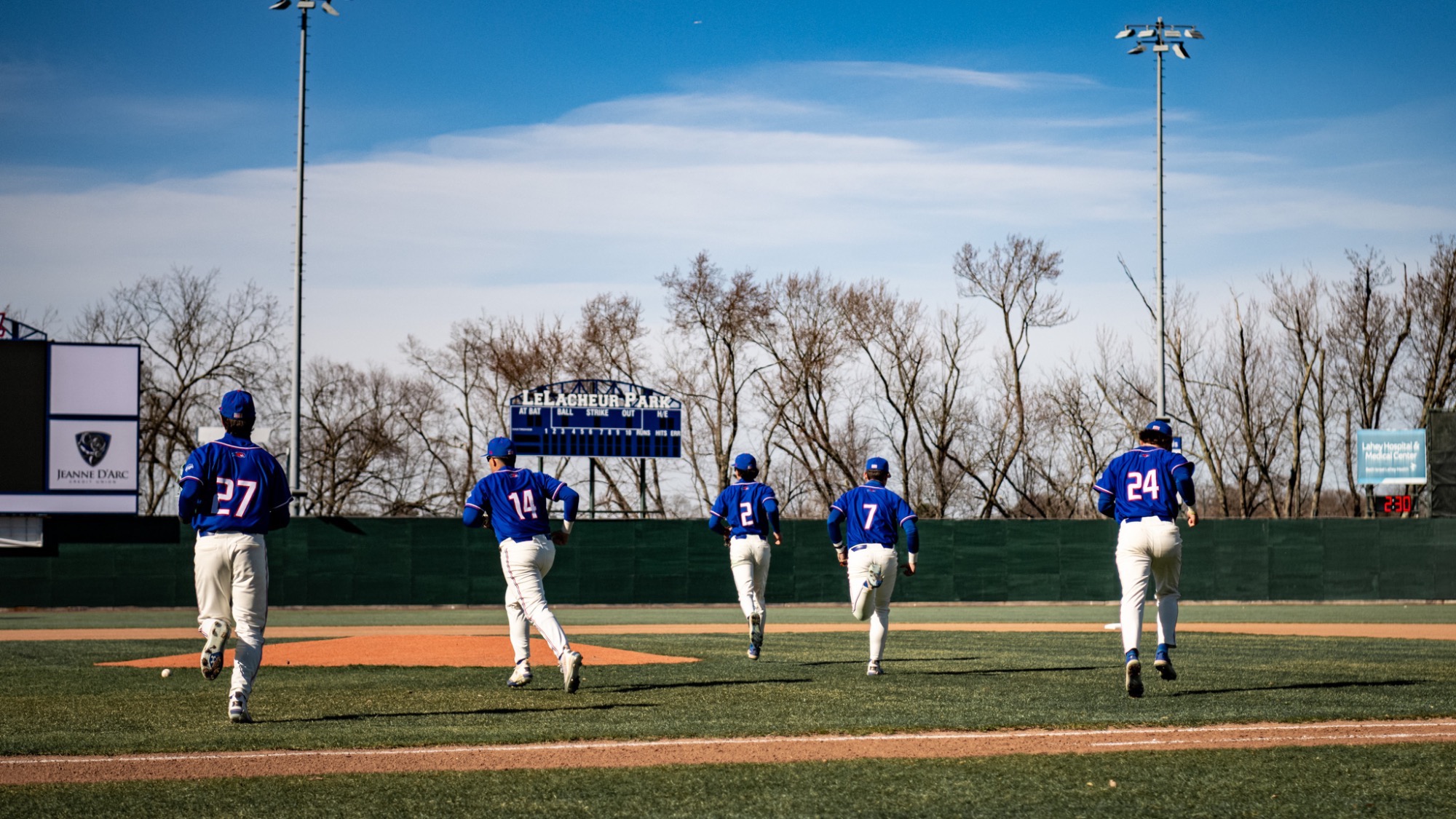 UMass Lowell baseball players running onto Edward A. LeLacheur Park's field to warm up before the start of an inning against the Northeastern Huskies on March 25, 2026
