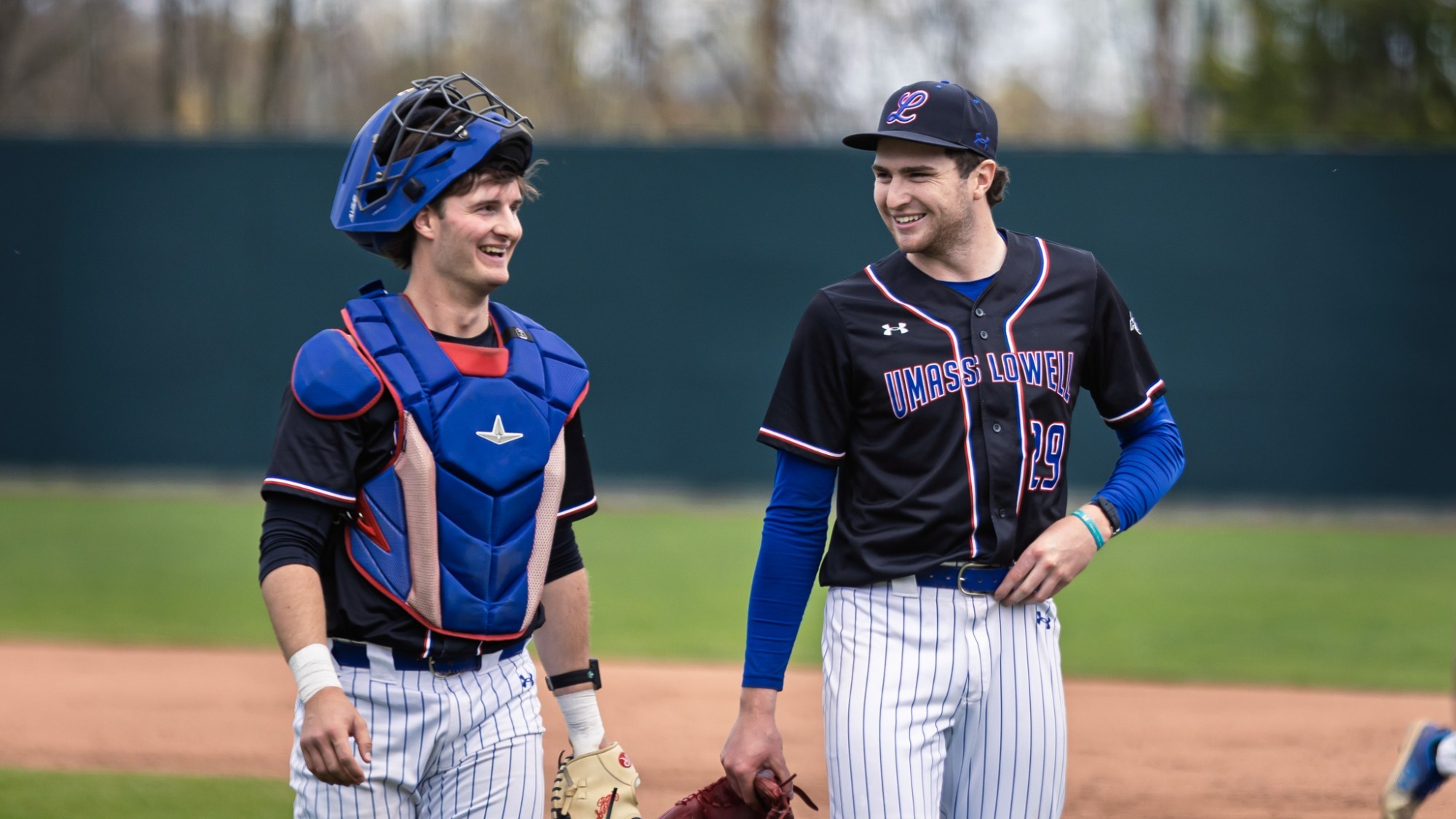 UMass Lowell Baseball players smiling as they walk back to the dugout after ending the half inning on the field