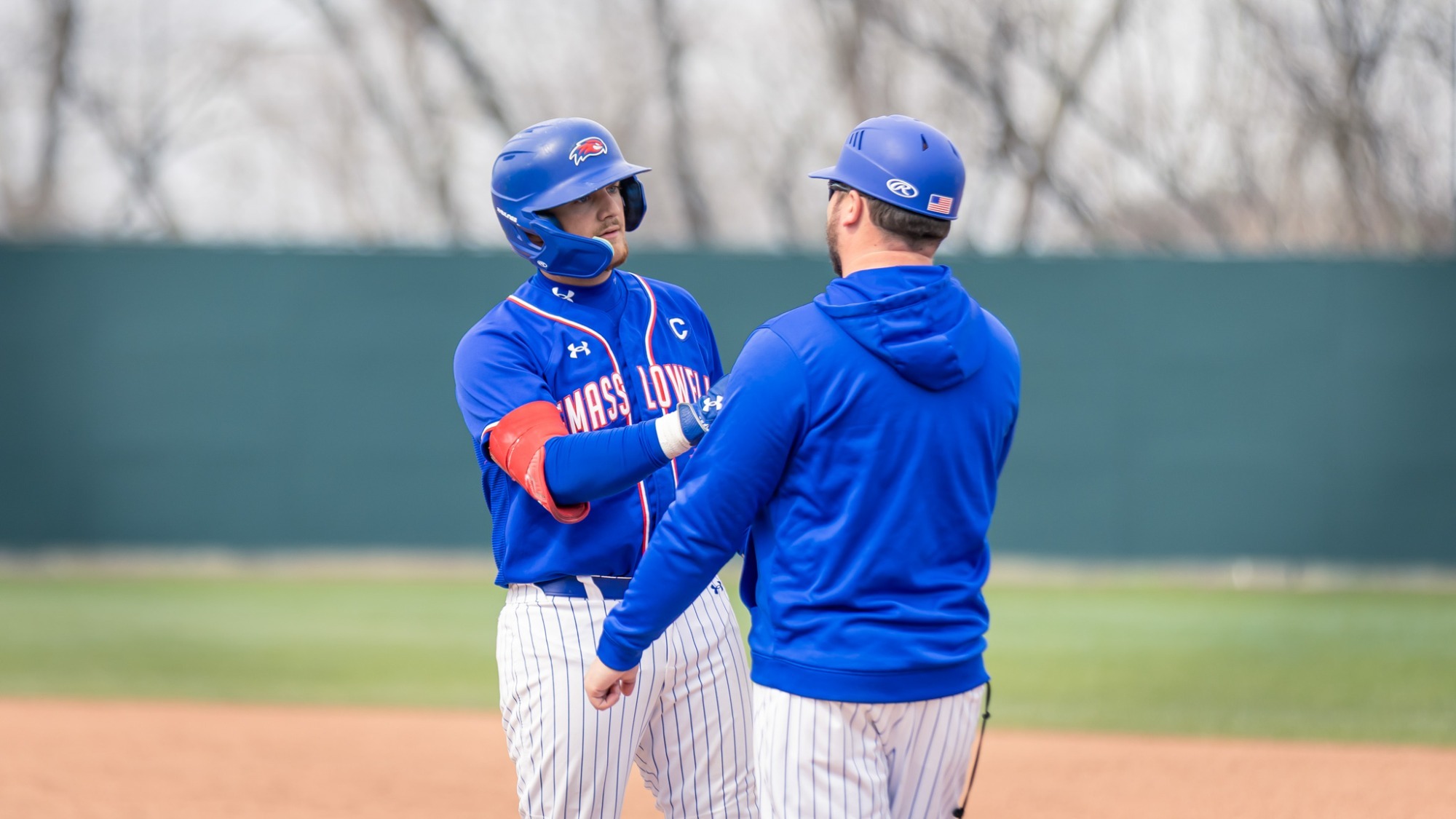 UMass Lowell baseball player and a coach at first base after the batter reached base