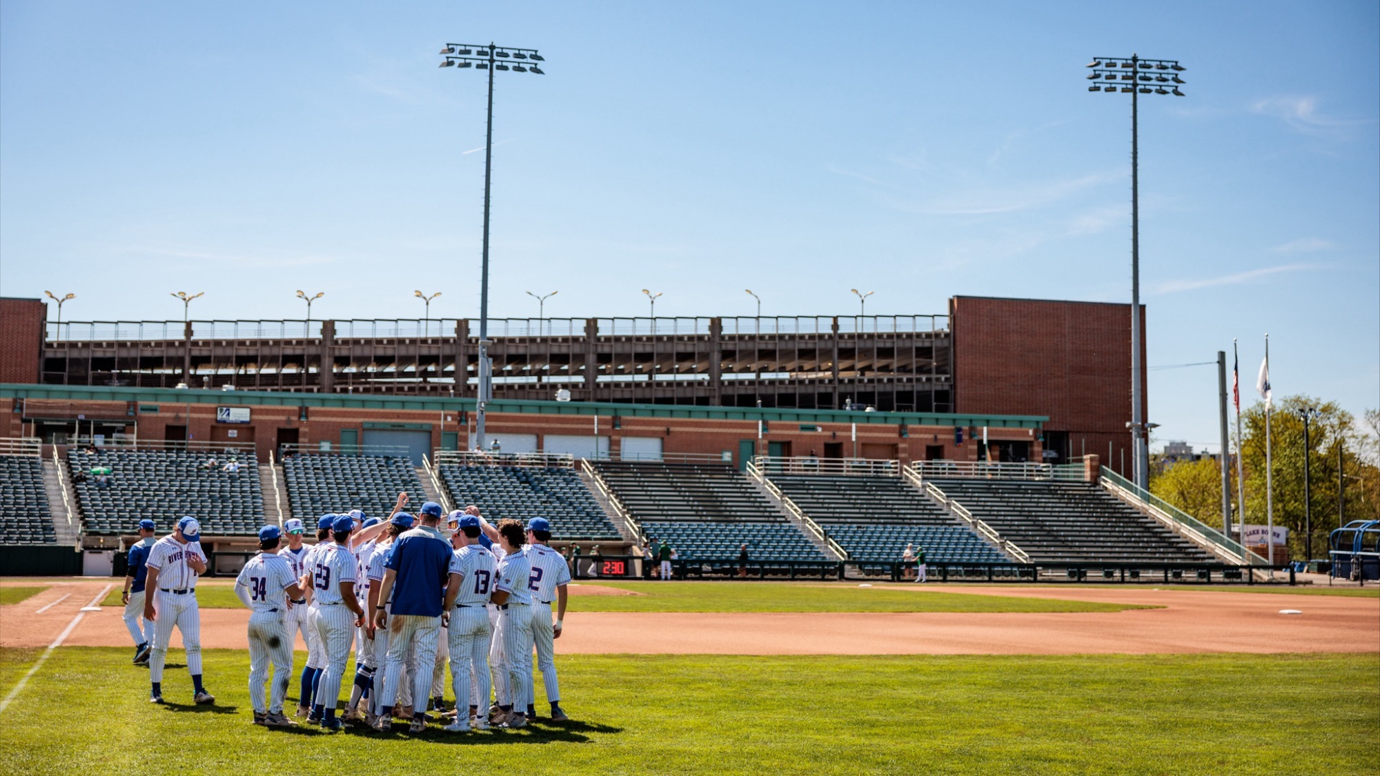 UMass Lowell baseball team in a small huddle on LeLacheur Park pregame