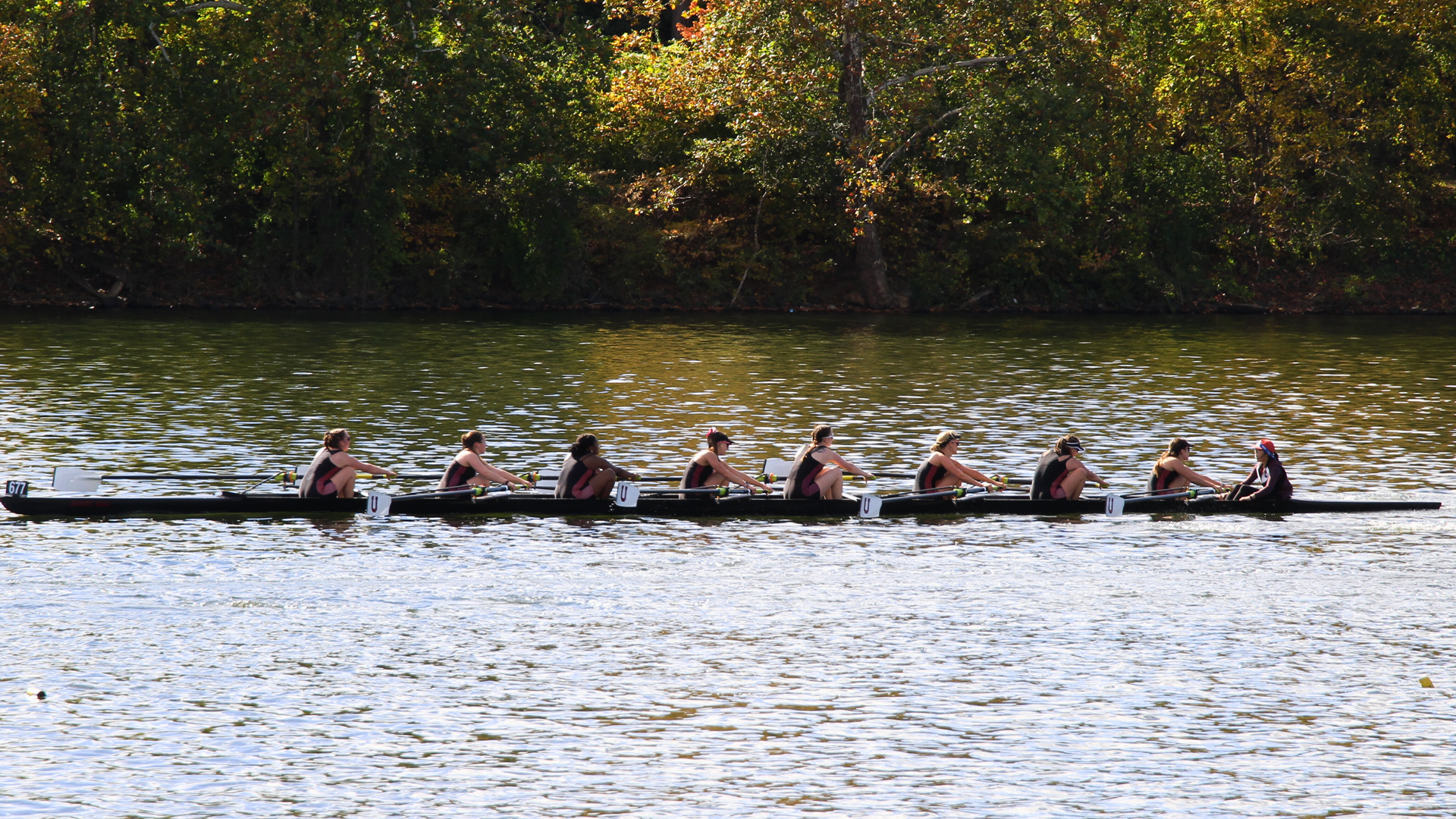 Union's women's collegiate 8+ boat on the water rowing from right to left