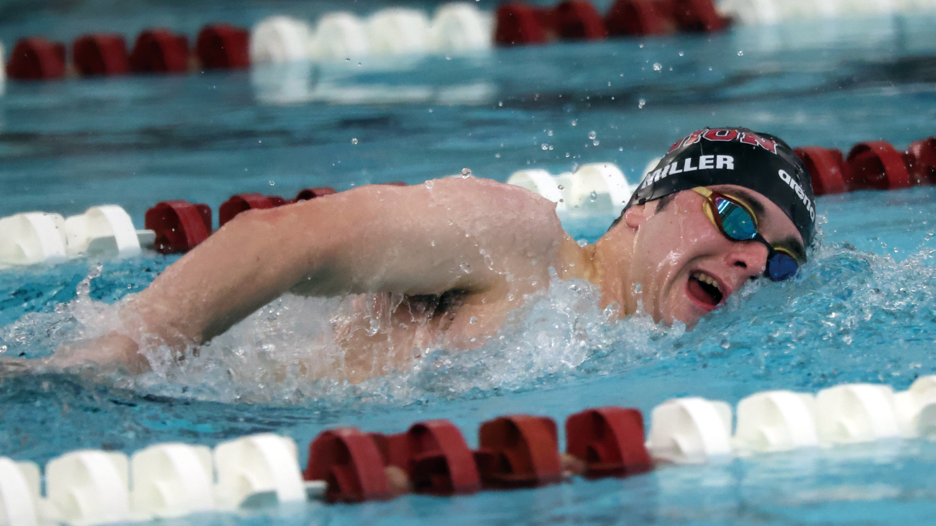 a men's swimmer swimming the front crawl with a black swim cap on that reads 