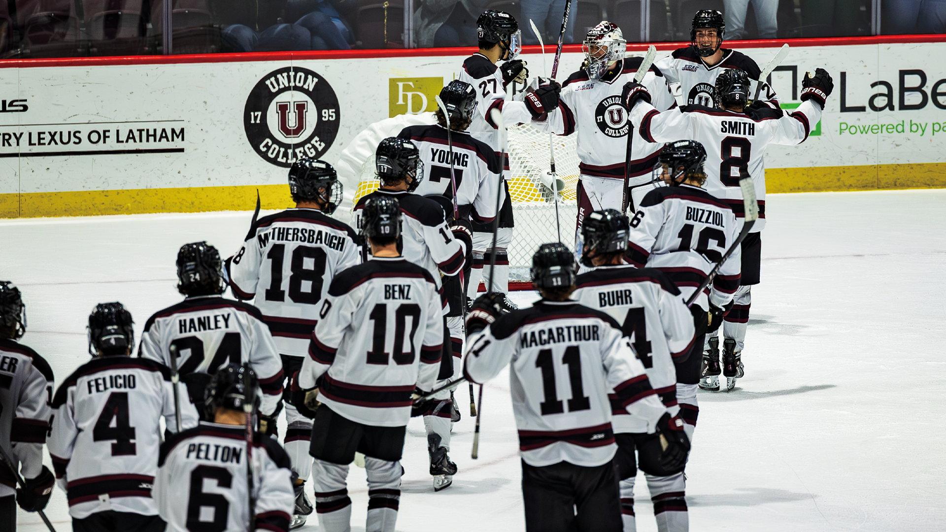 men's hockey players lining up on the ice to go congratulate their goalie after a win. The players are wearing white jerseys and black helmets