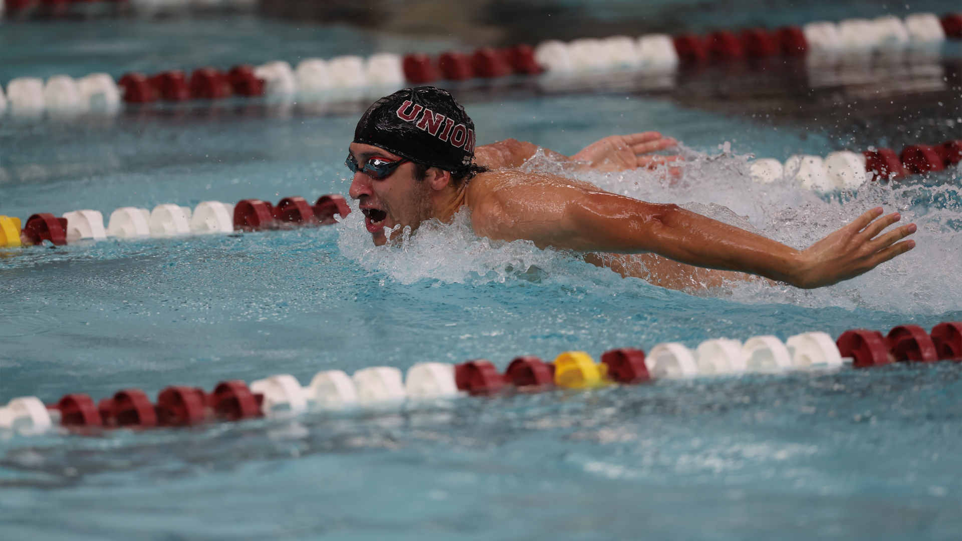 men's swimmer performing the butterfly, wearing a black swim cap that reads 