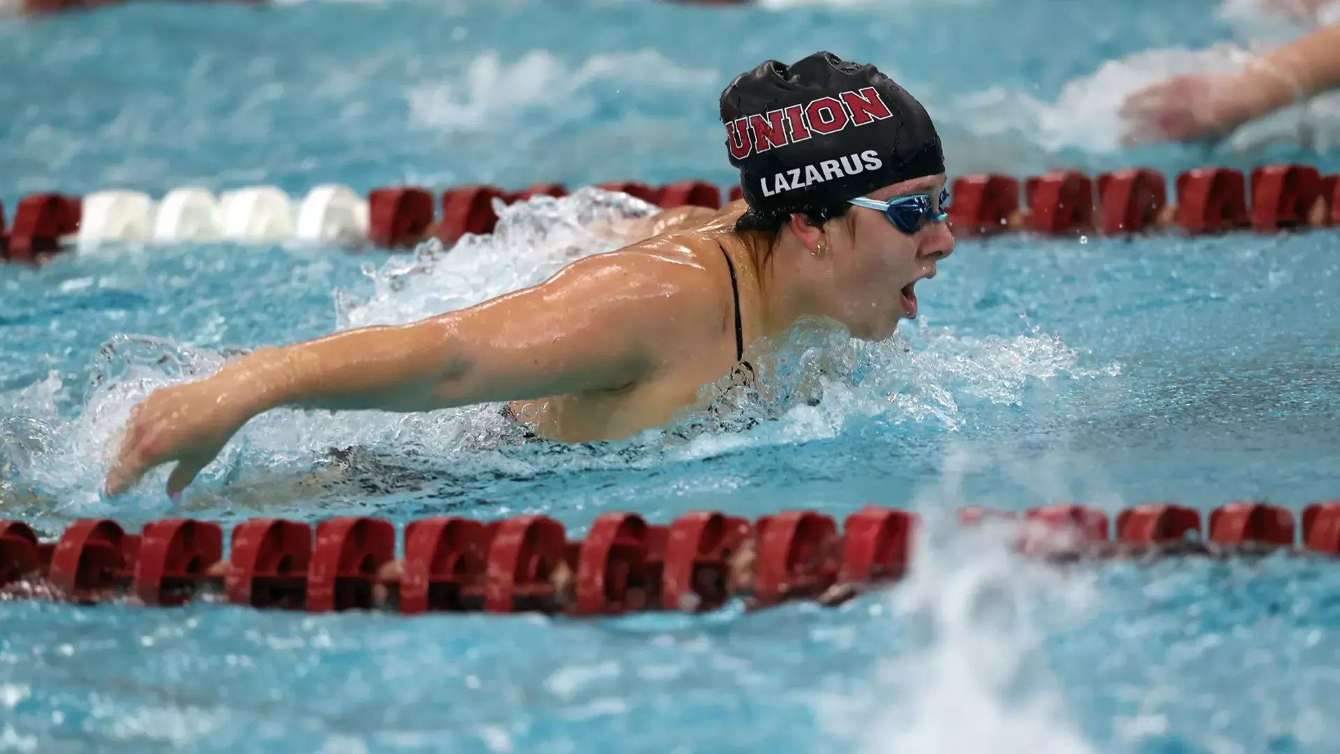 women's swimmer performing the butterfly stroke, wearing a black swim cap that reads 