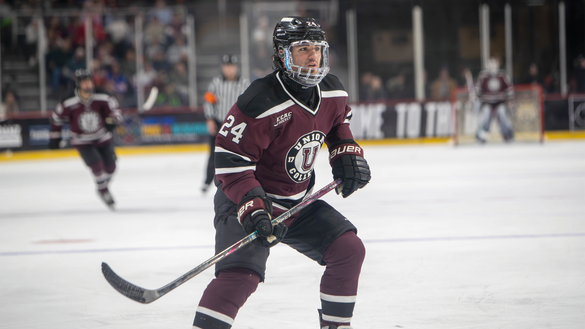 a men's hockey player skating backwards wearing a garnet jersey, looking to his left
