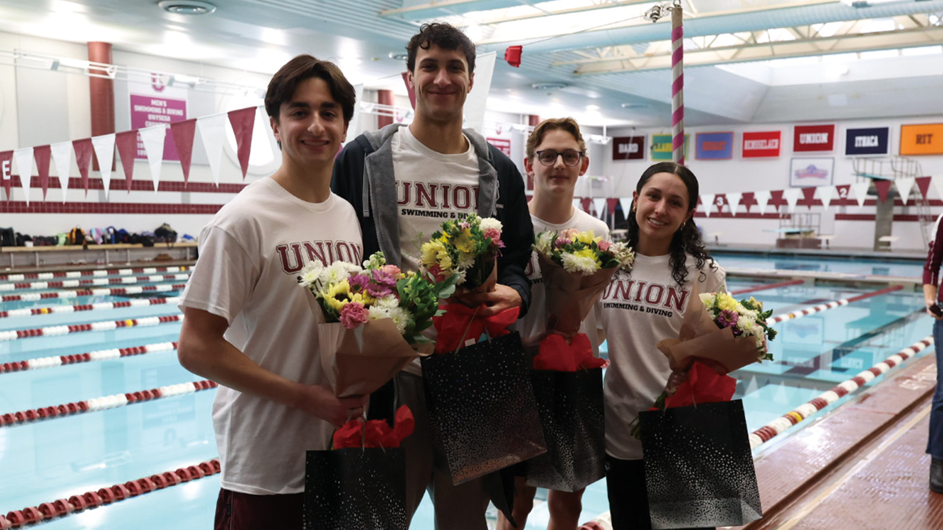four swimmers standing poolside holding flowers and gift bags they received on their senior day. 